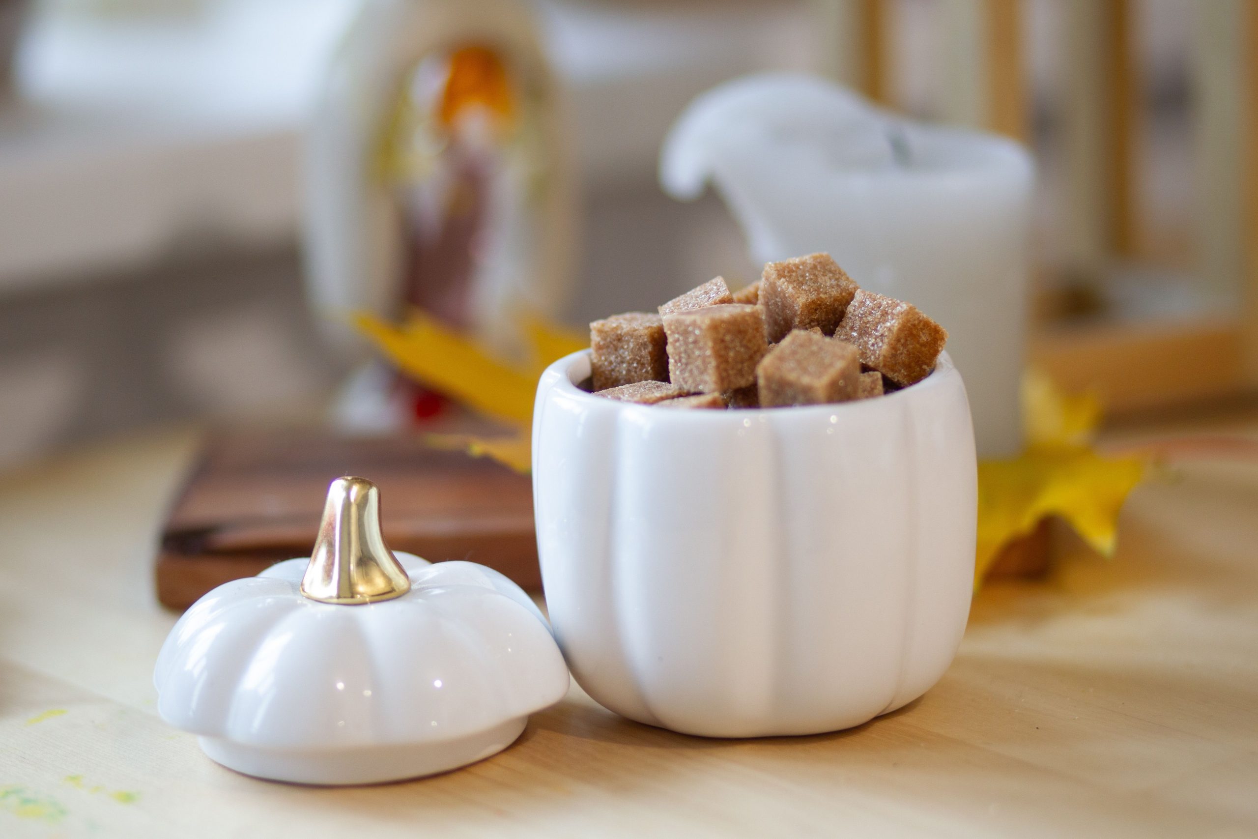 A pumpkin-shaped holder filled with sugar cubes, with an autumn decor background.