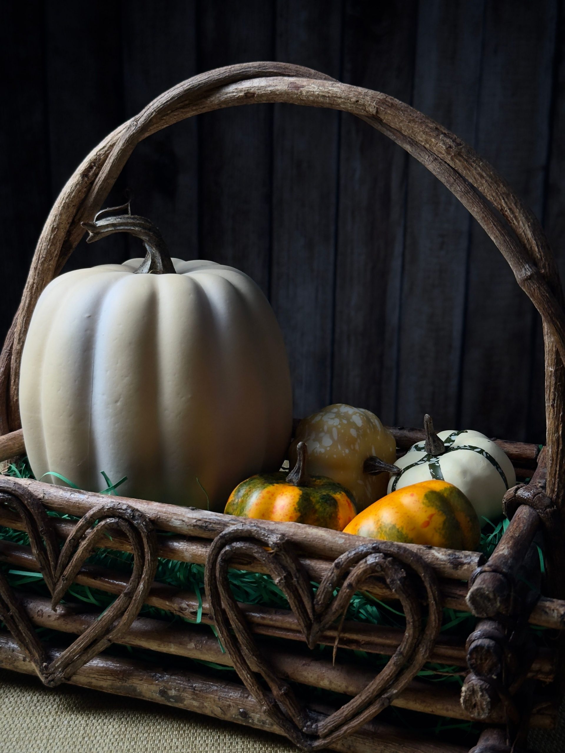 A rustic wicker basket filled with decorative pumpkins and gourds, set against a wooden backdrop.