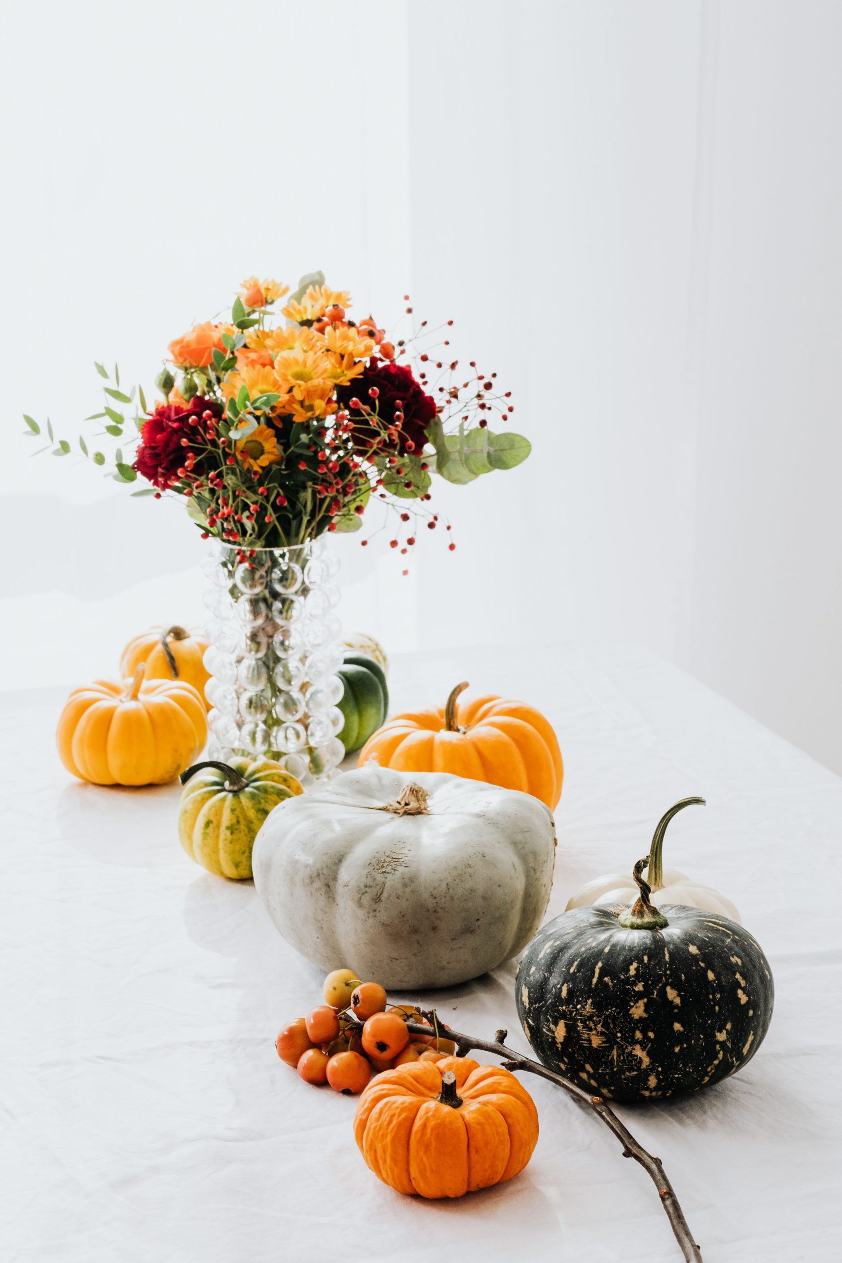 A serene autumn still life with pumpkins and vibrant floral arrangement in a glass vase.