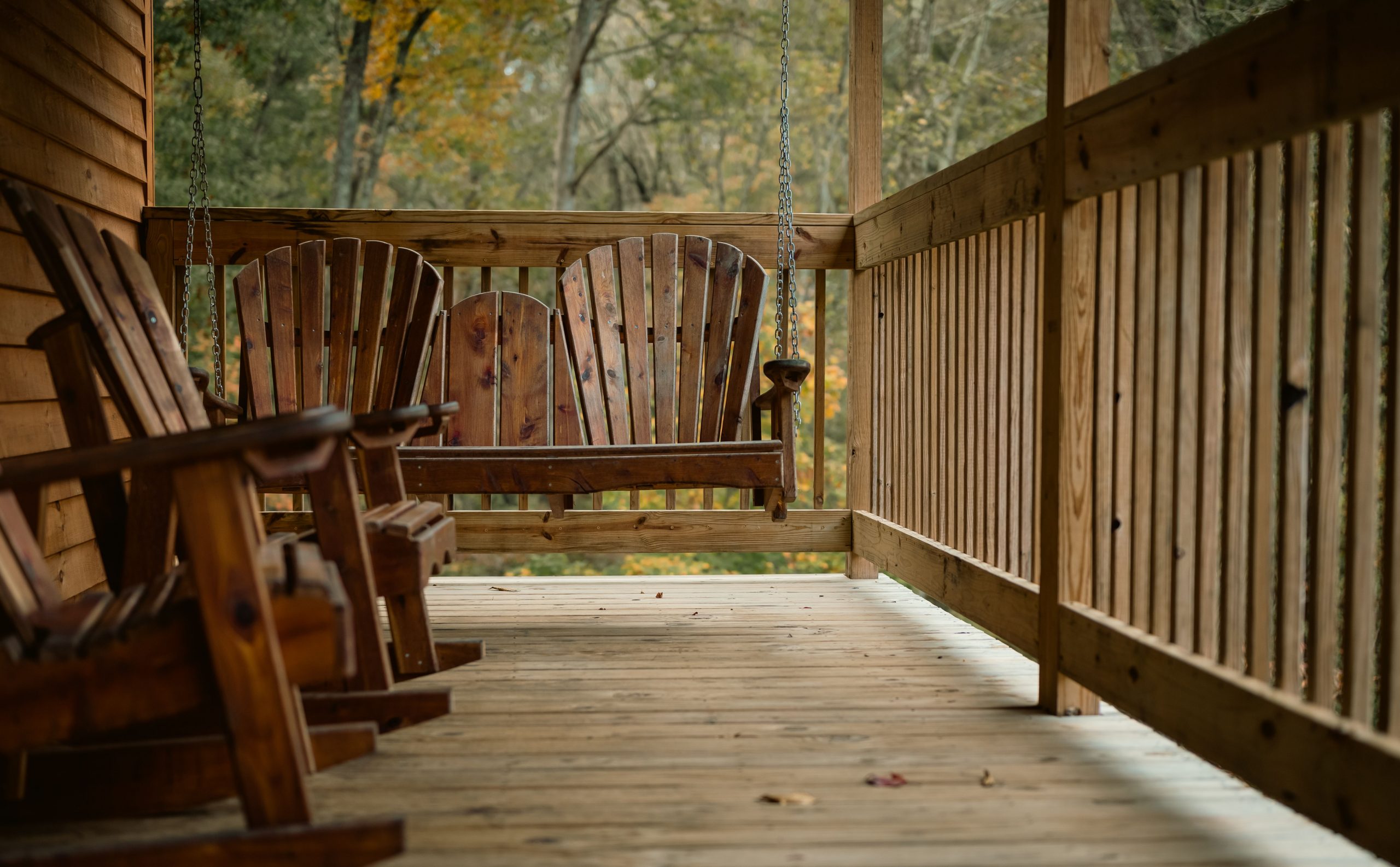A serene wooden porch featuring a rustic hanging swing amidst autumnal foliage.