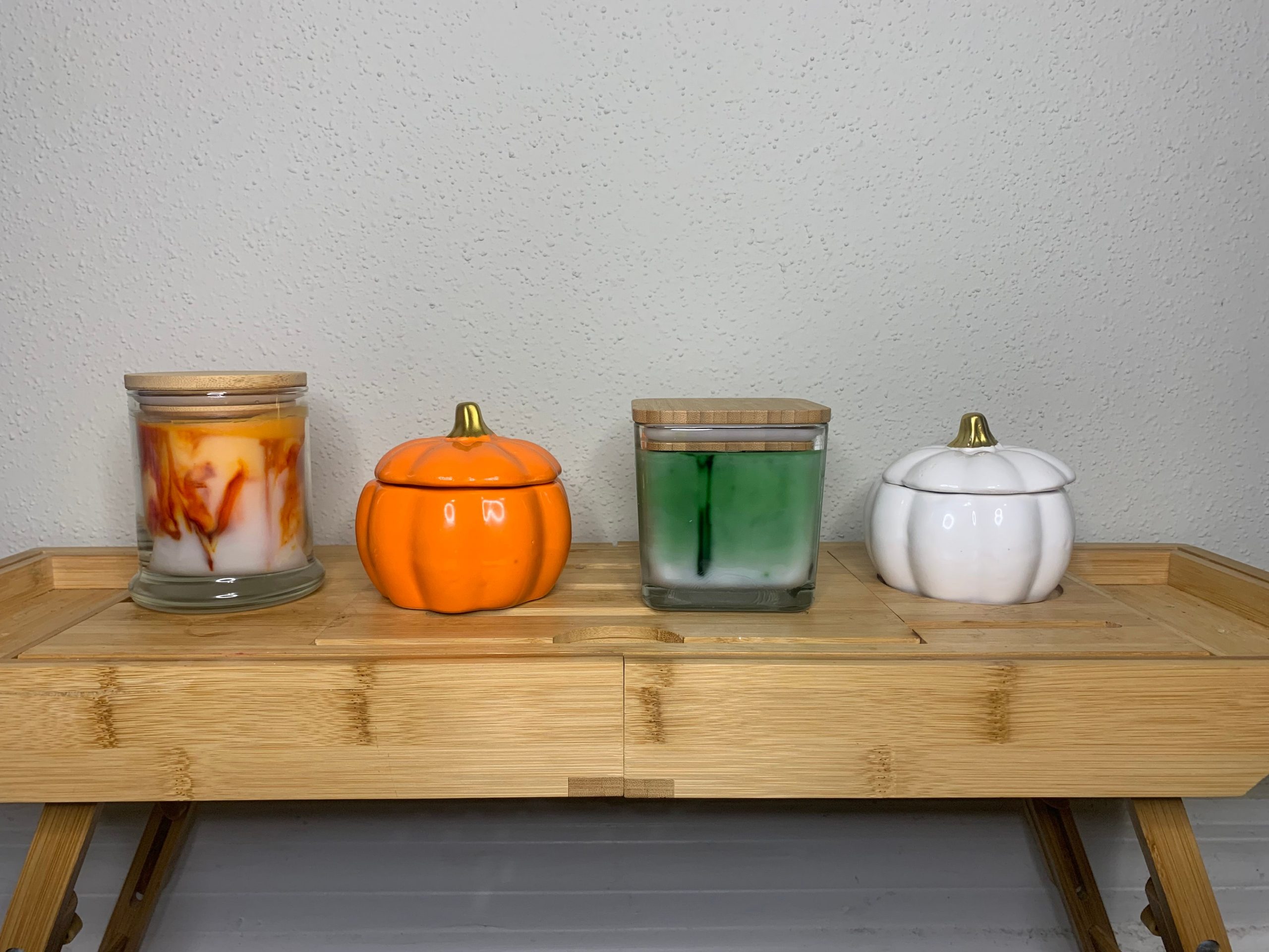 A set of decorative pumpkin-shaped and glass candles on a bamboo table.
