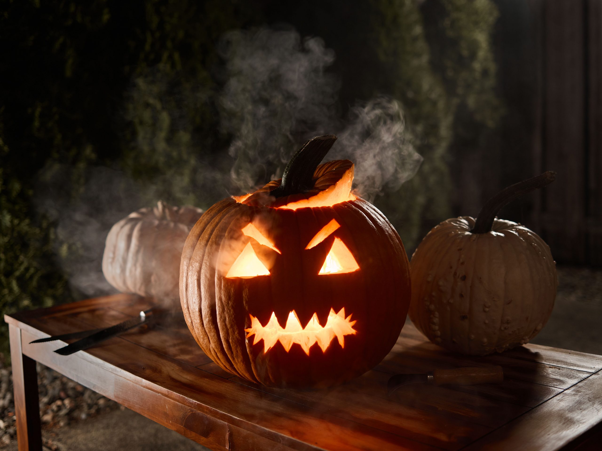 A spooky Jack-o'-lantern emits a warm glow illuminating a wooden table during Halloween night.
