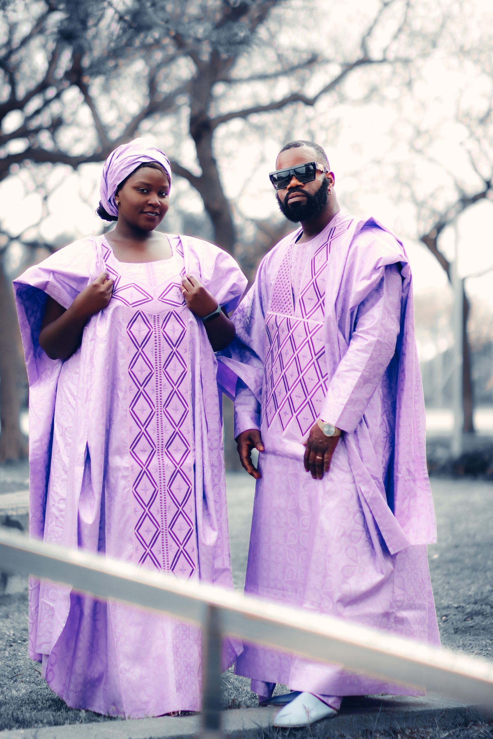 A stylish couple wearing matching vibrant traditional African clothing, posing together outdoors.