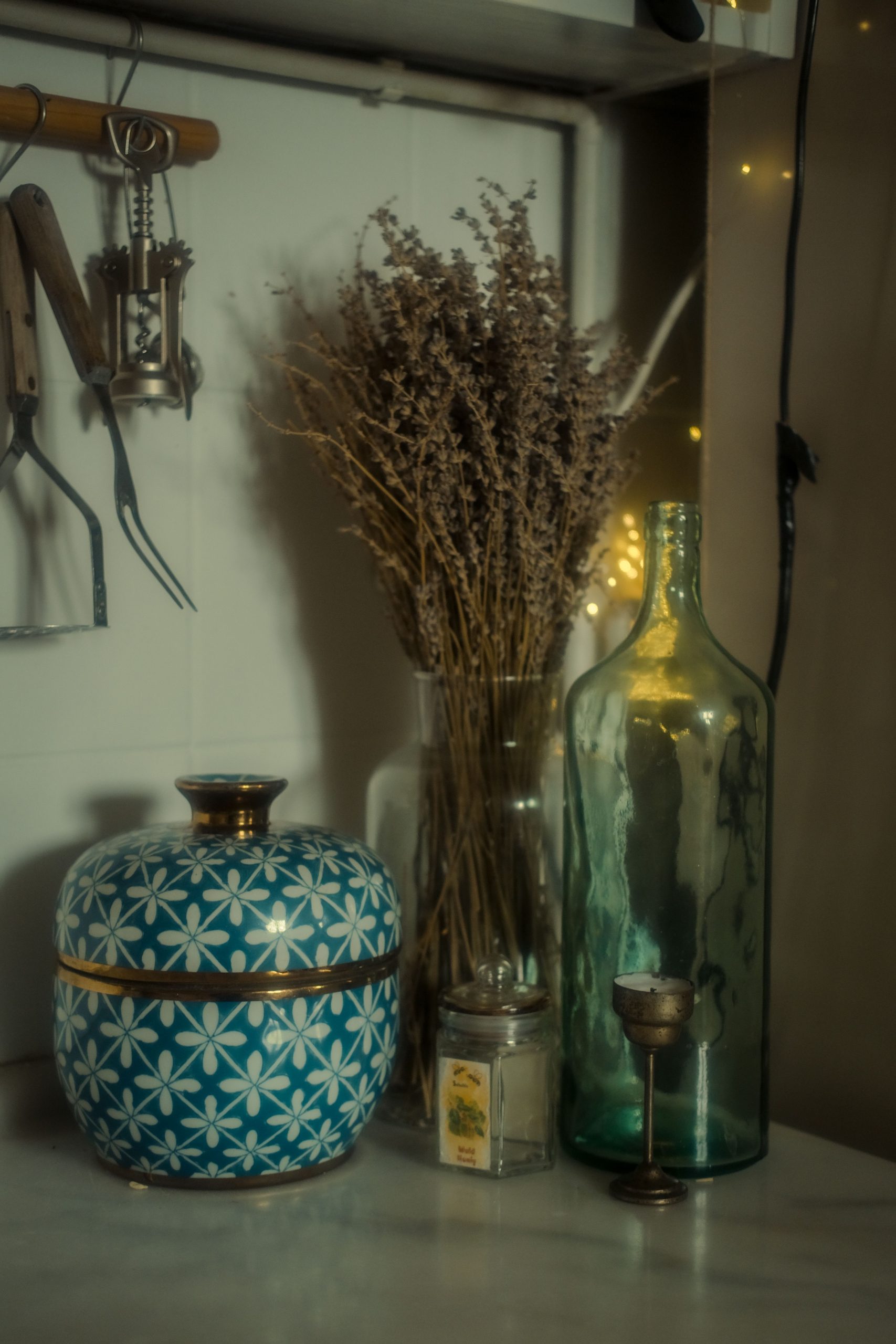 A vintage kitchen scene with a porcelain jar, dried flowers, and a glass bottle on a countertop.