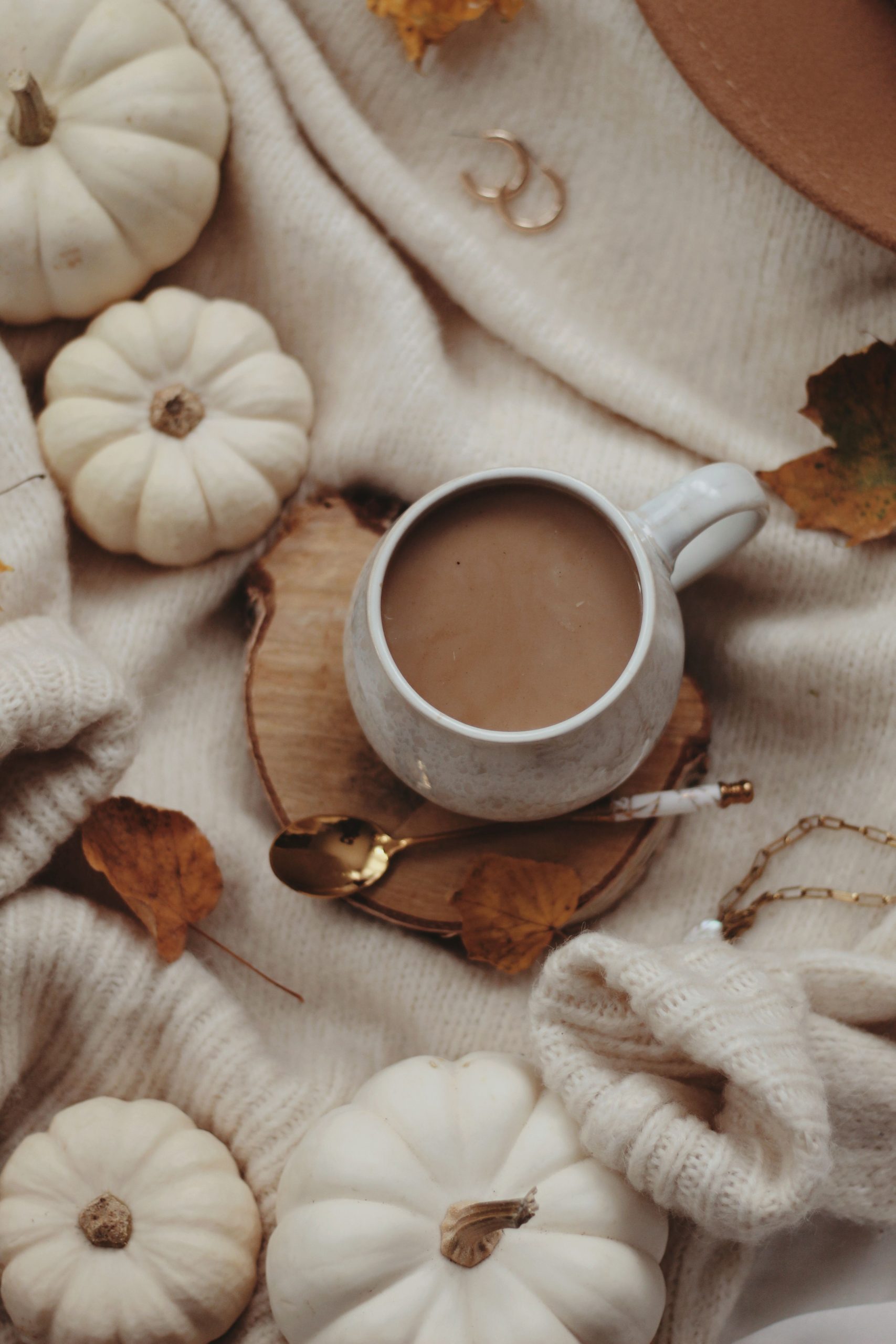 A warm autumn scene with a ceramic mug of coffee surrounded by mini pumpkins and leaves.