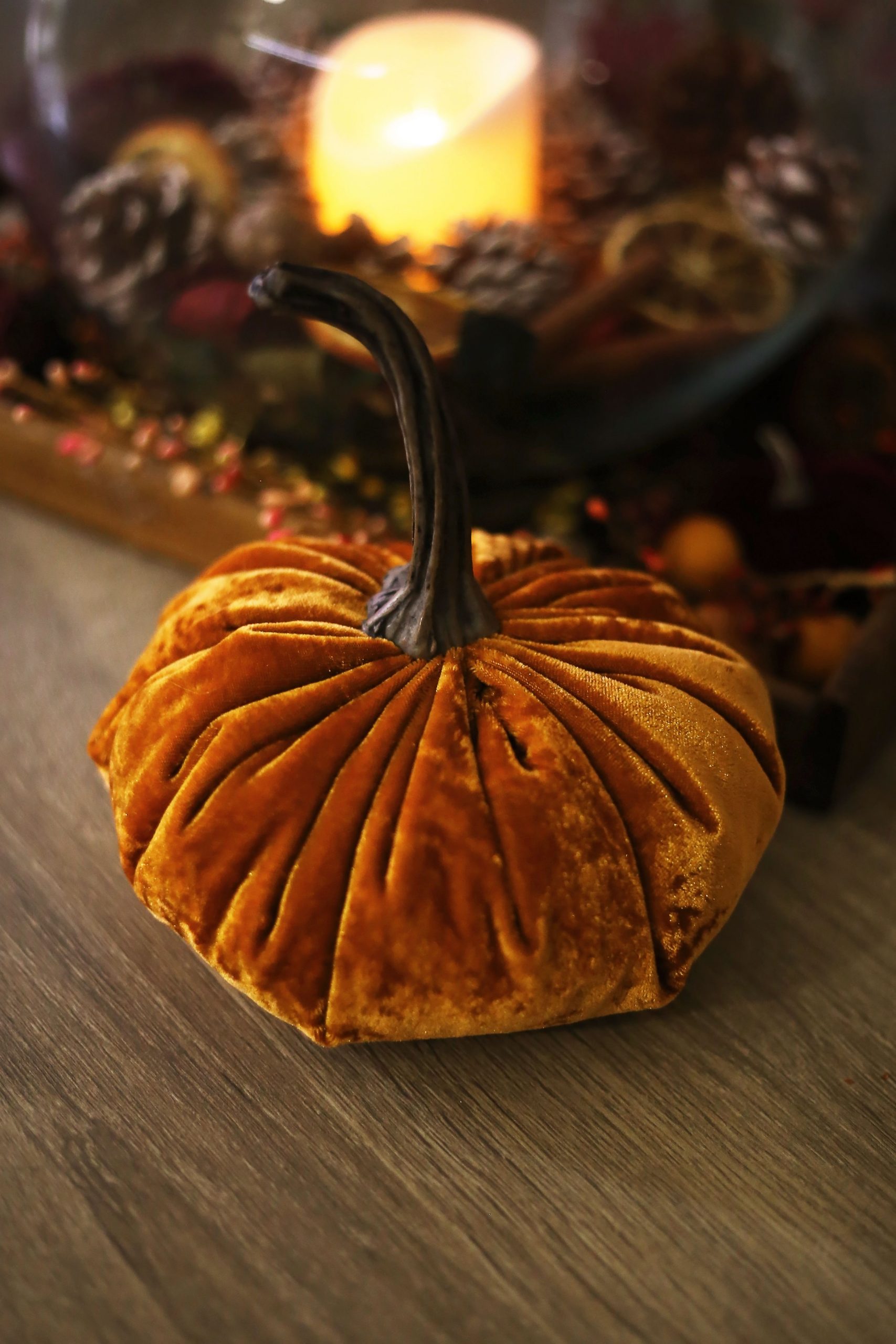 A warm, autumn-themed composition featuring a velvet pumpkin and candle on a wooden surface.