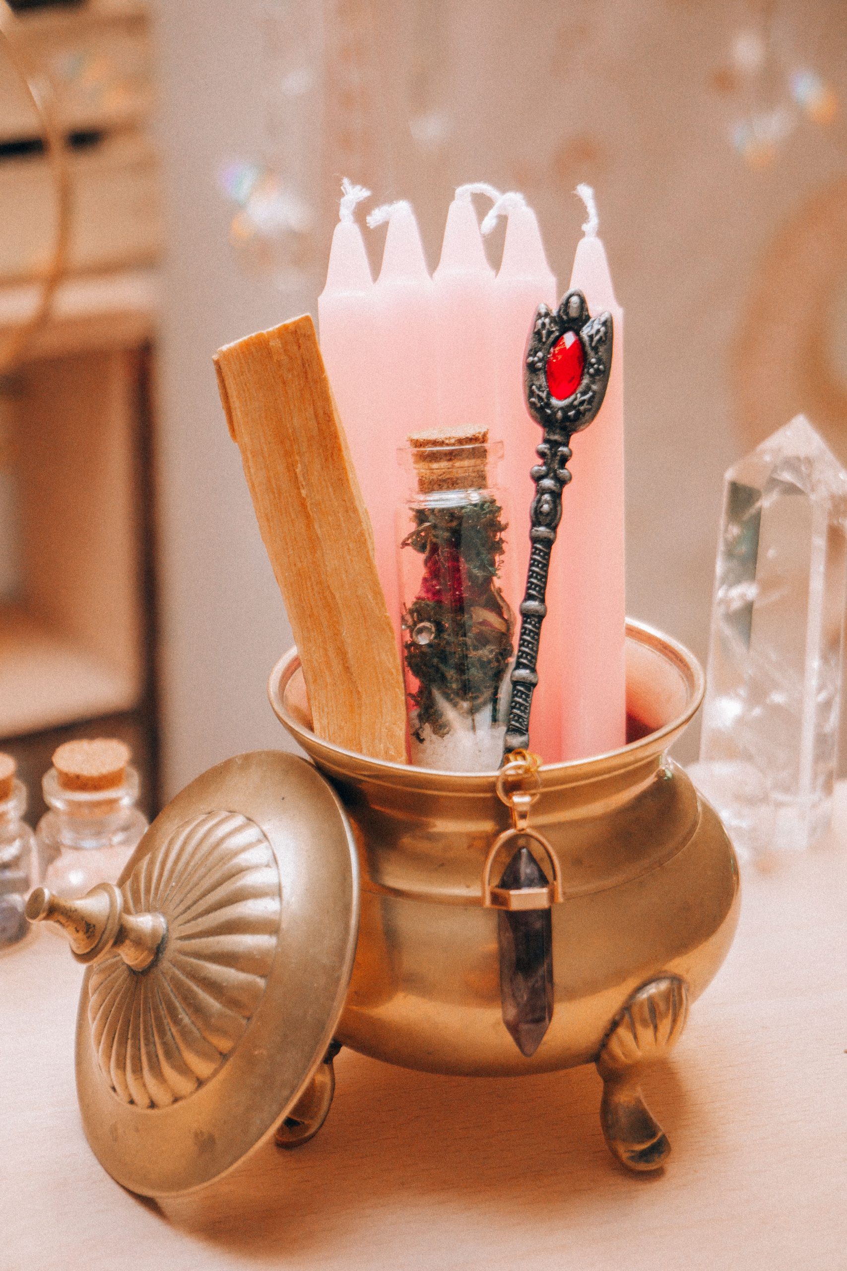 A witchy arrangement with pink candles, crystal vial, and incense in a vintage pot.