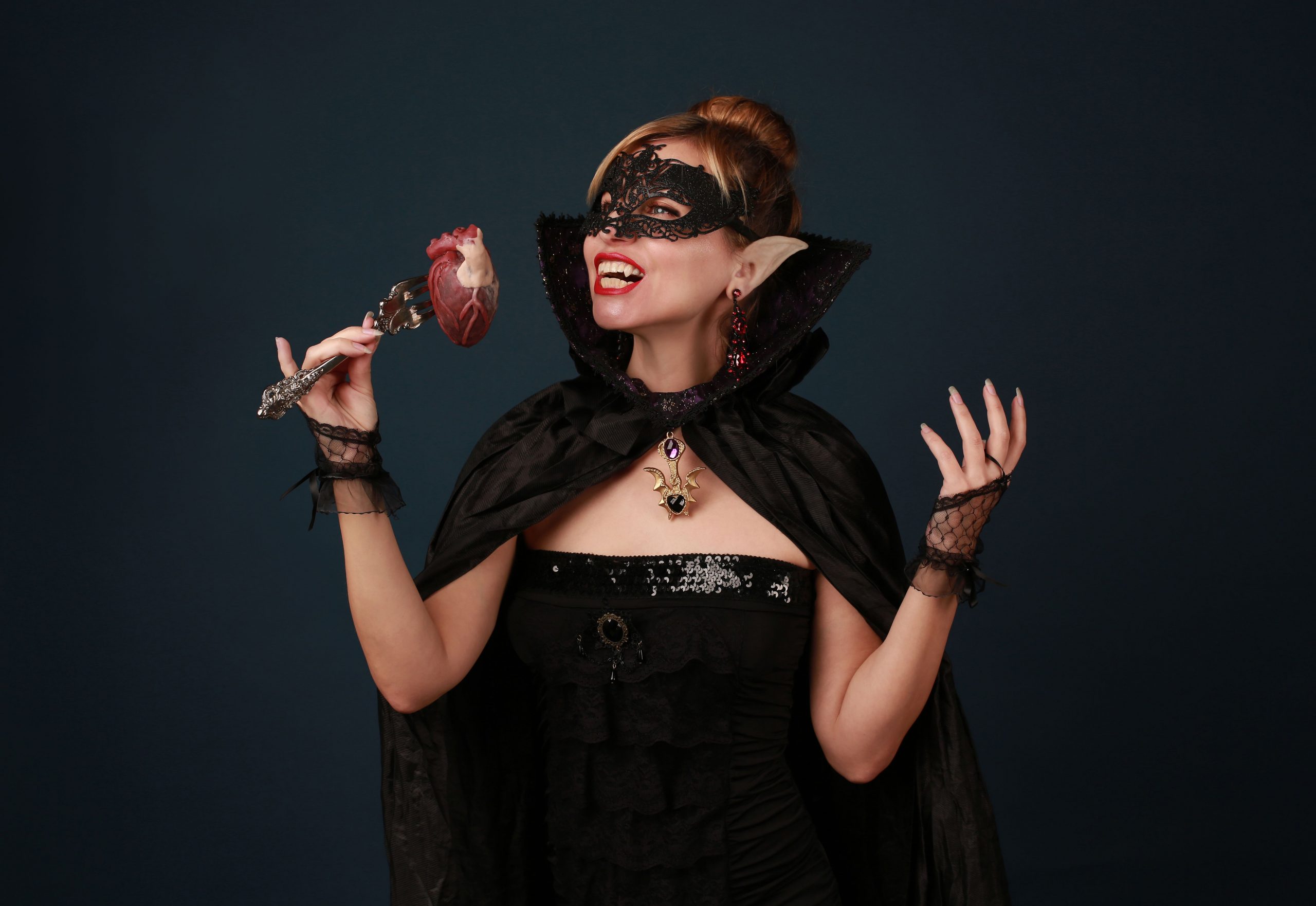 A woman dressed as a vampire enjoying Halloween with a heart prop in hand.