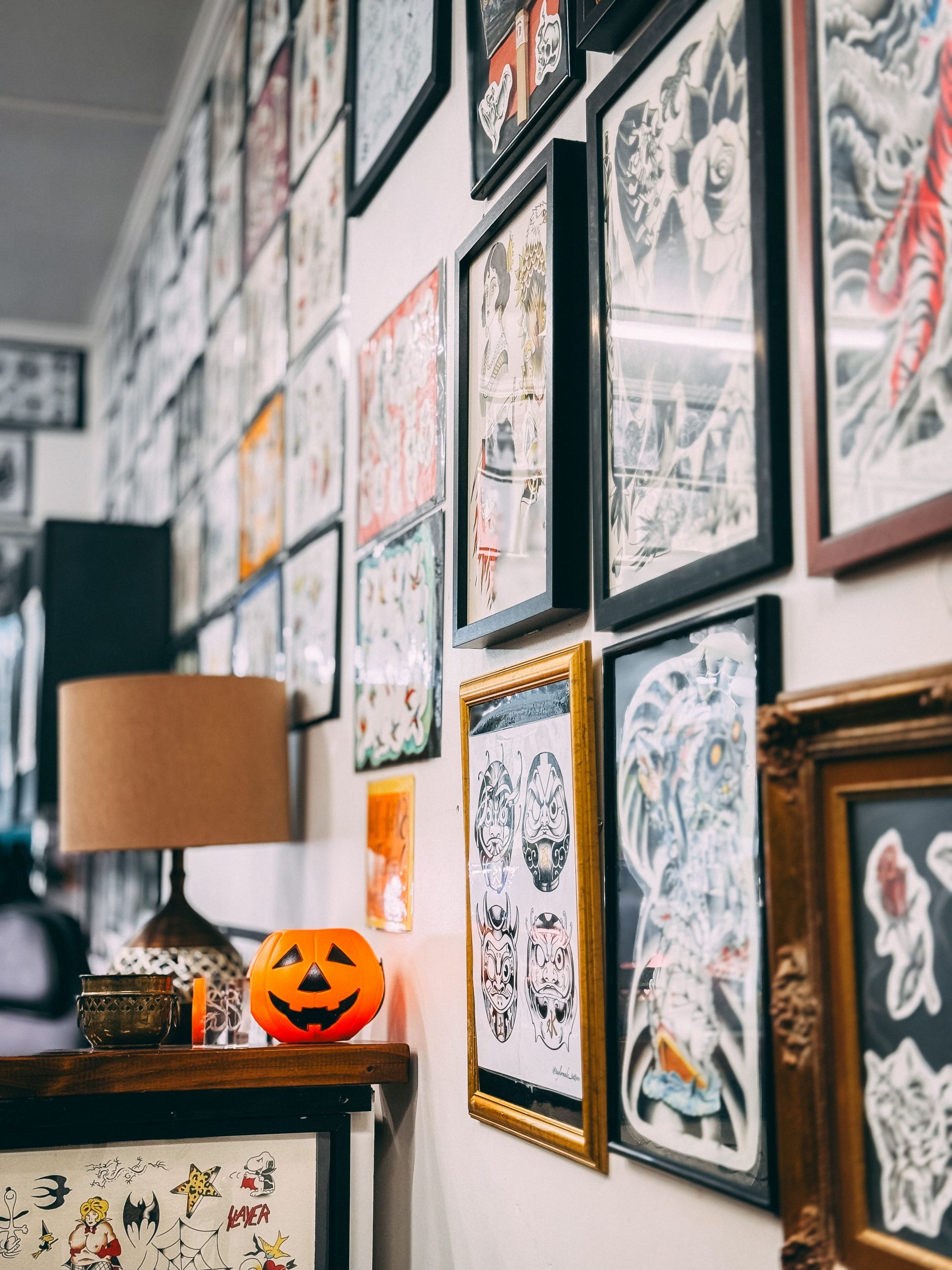 An artistic tattoo parlor wall adorned with various framed artworks and a Halloween-themed pumpkin.