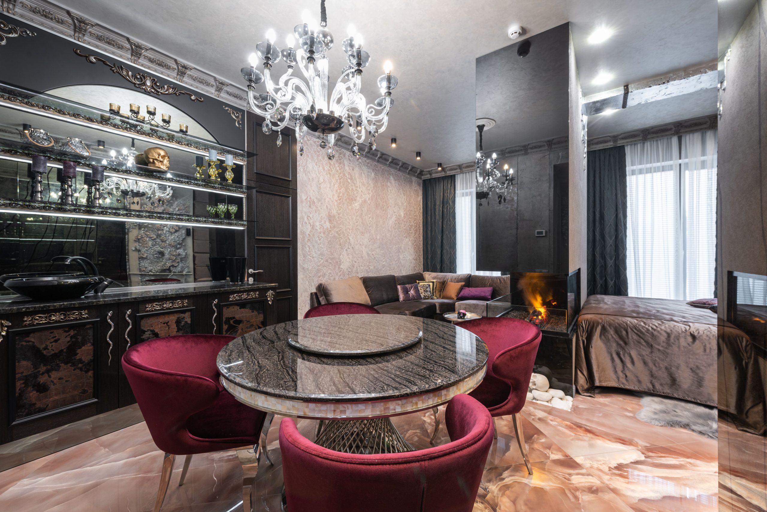 Armchairs at table placed near kitchen counter with kitchenware in modern spacious apartment with bed near burning fireplace and couch