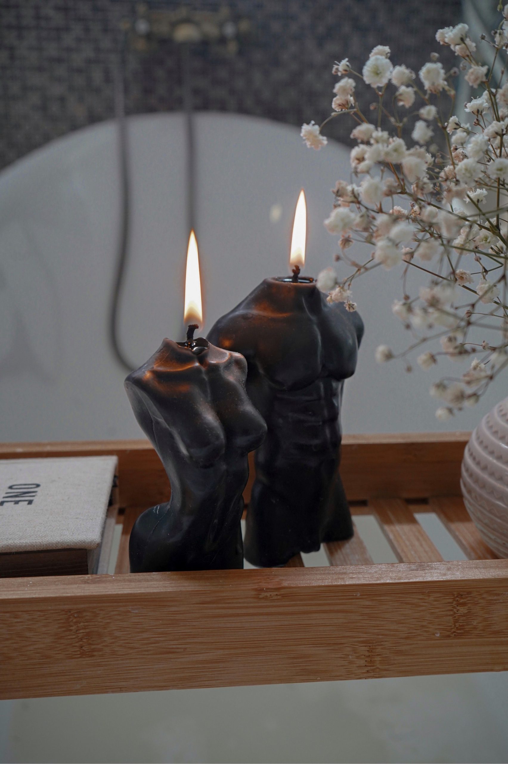 Artistic candles shaped like human torsos, accompanied by delicate flowers, create a serene atmosphere.