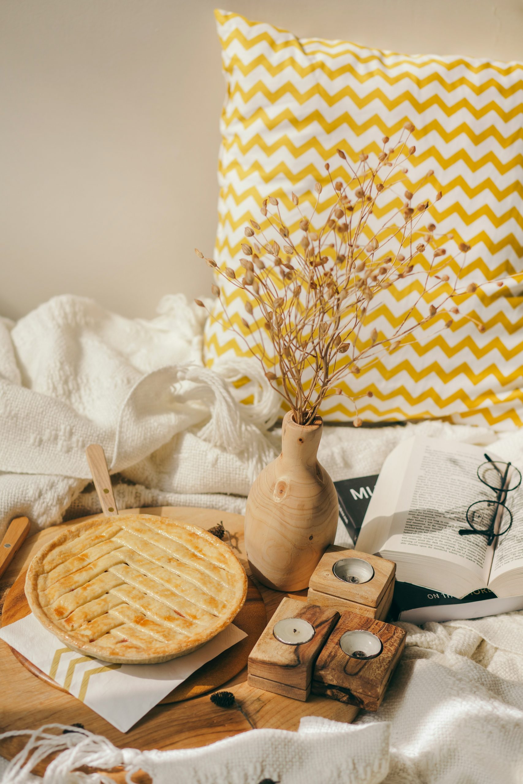 Autumn pie, candle, and book knitted textile in bed, Winter holiday season. Cozy breakfast in cold weather, piece of pie. cozy autumn still life with pumpkins tart, a knitted woolen blanket, and a boo