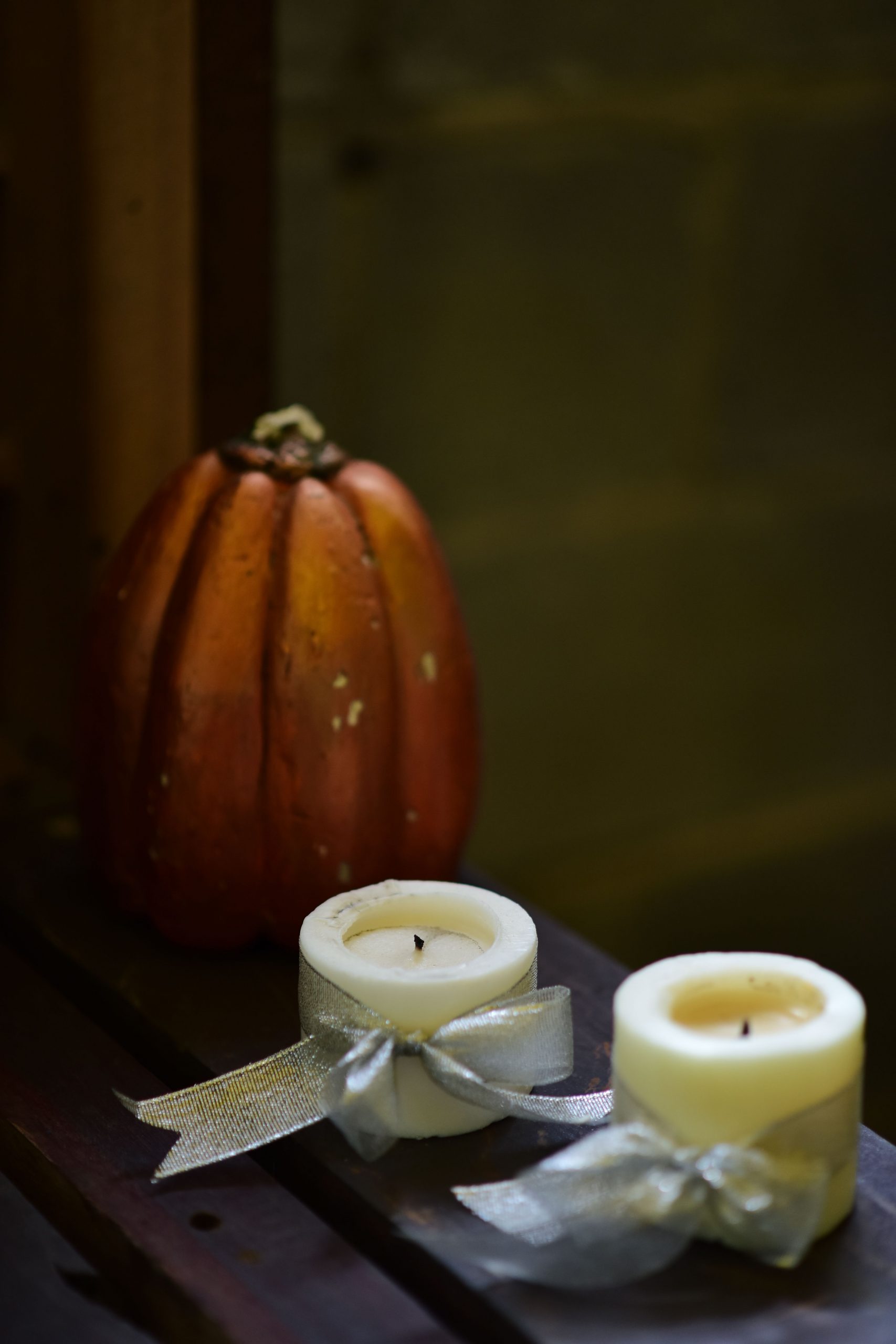 Autumn-themed setup with pumpkin and candles on a wooden surface in warm light.