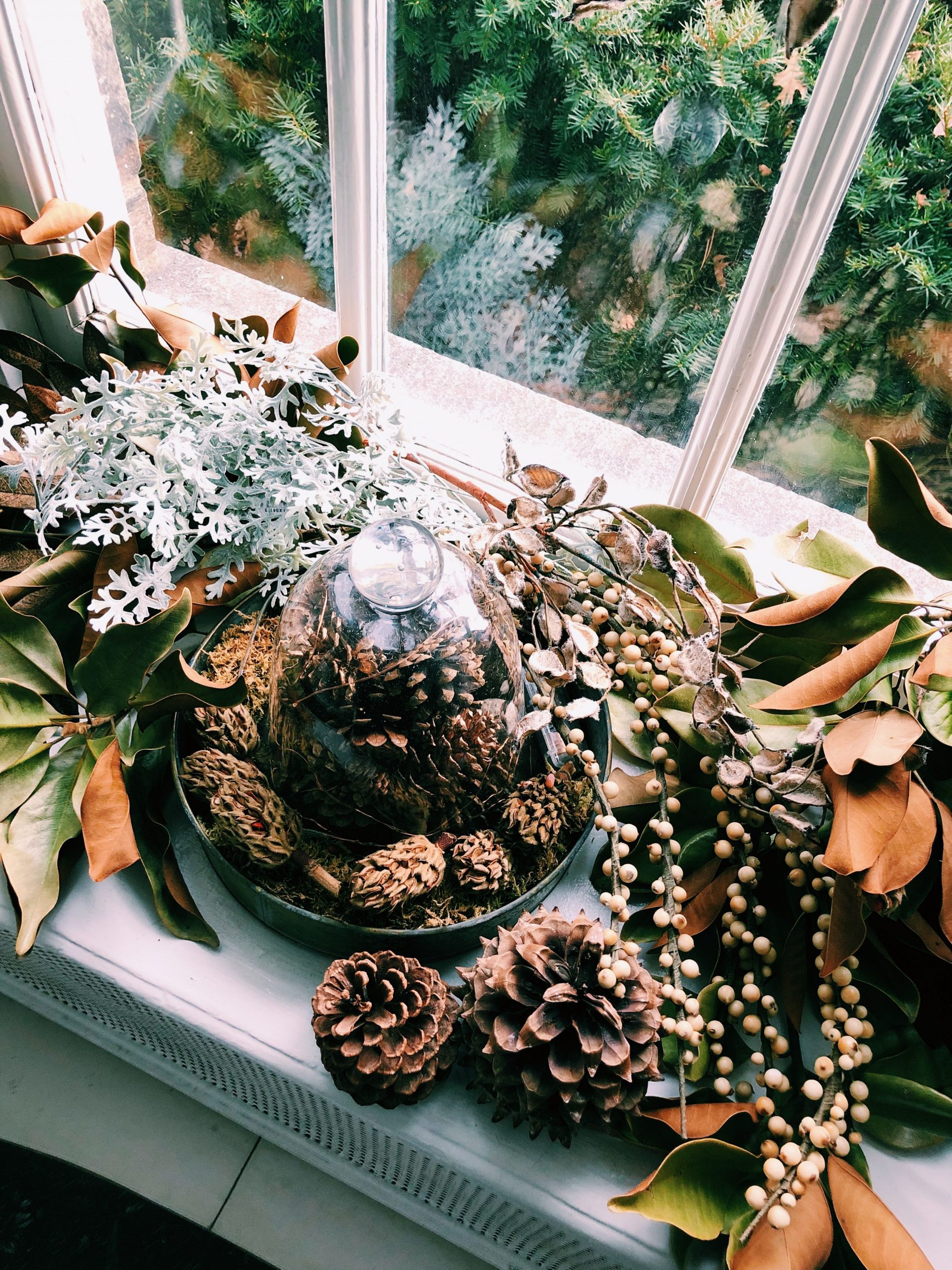 Autumn window sill arrangement featuring pine cones, leaves, and natural decorations.