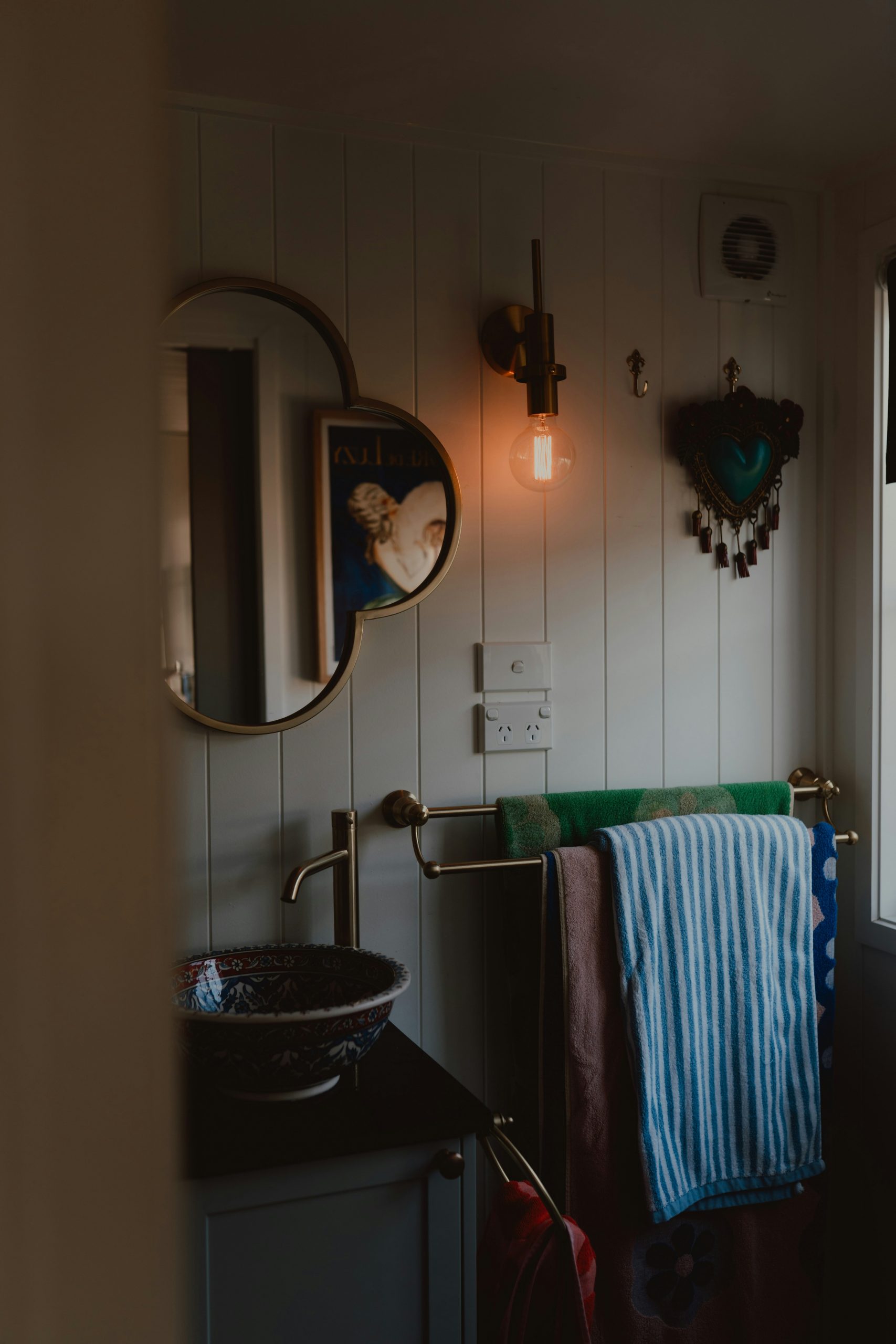 Bathroom with warm light, round mirror, decorative sink, and towels