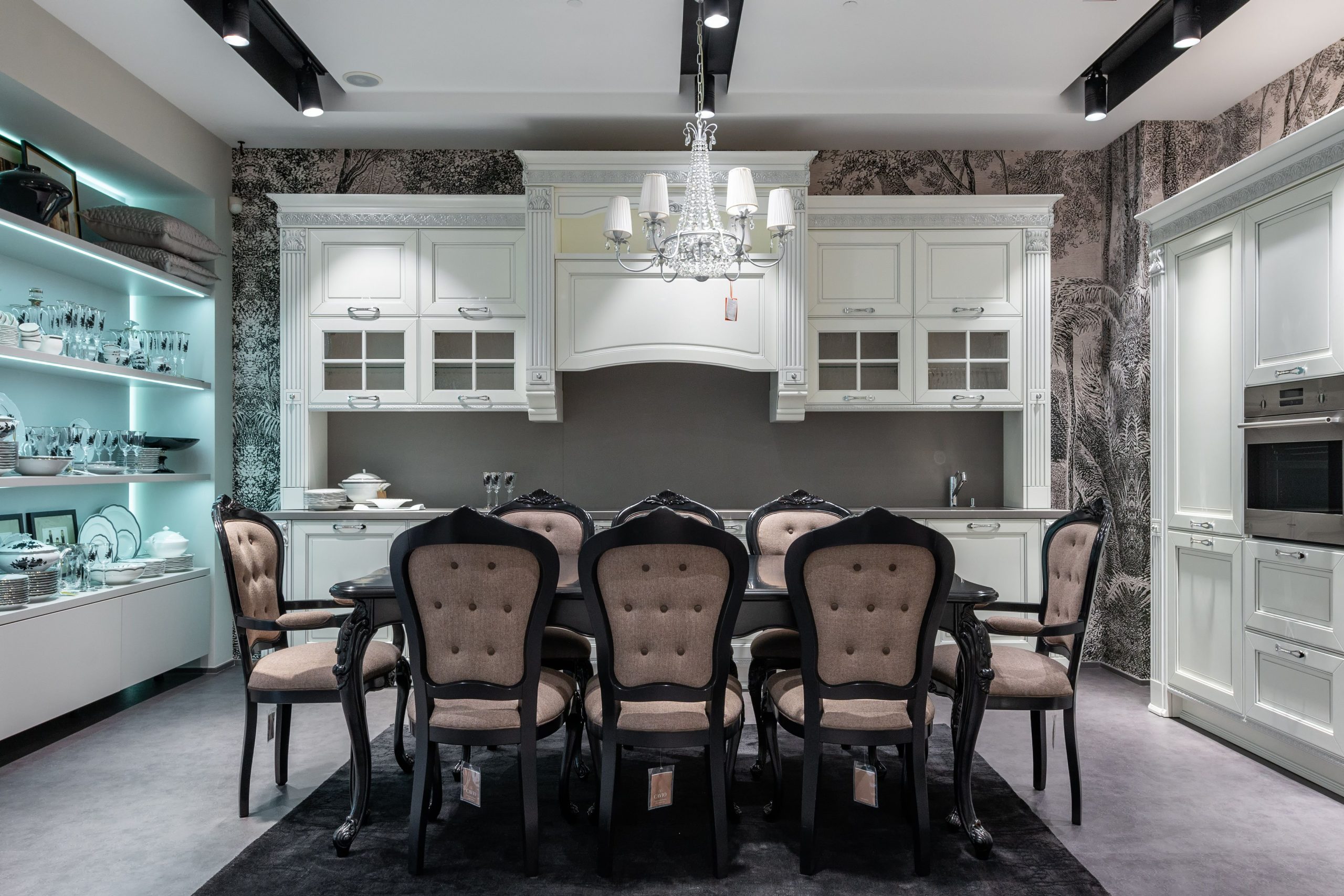 Chairs at table placed in spacious kitchen with oven near white cabinets and storage cupboard with various tableware in apartment