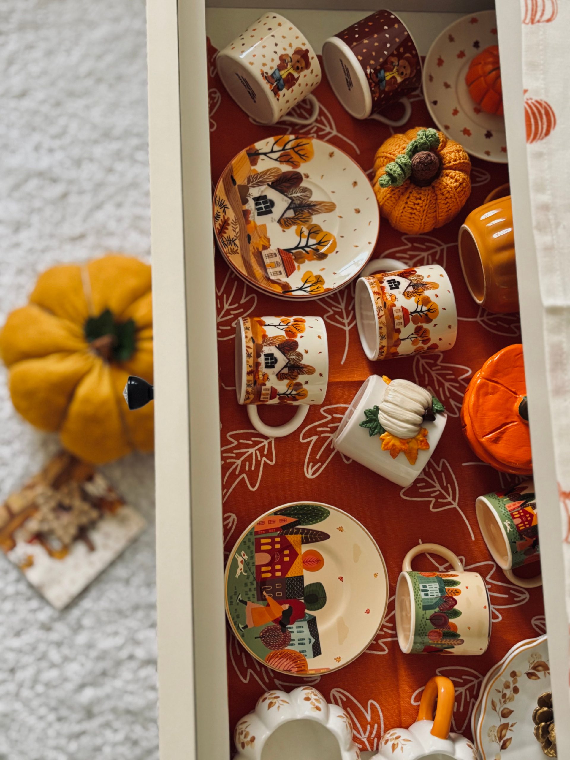Charming autumn-themed crockery with pumpkins and fall designs neatly arranged in a drawer.