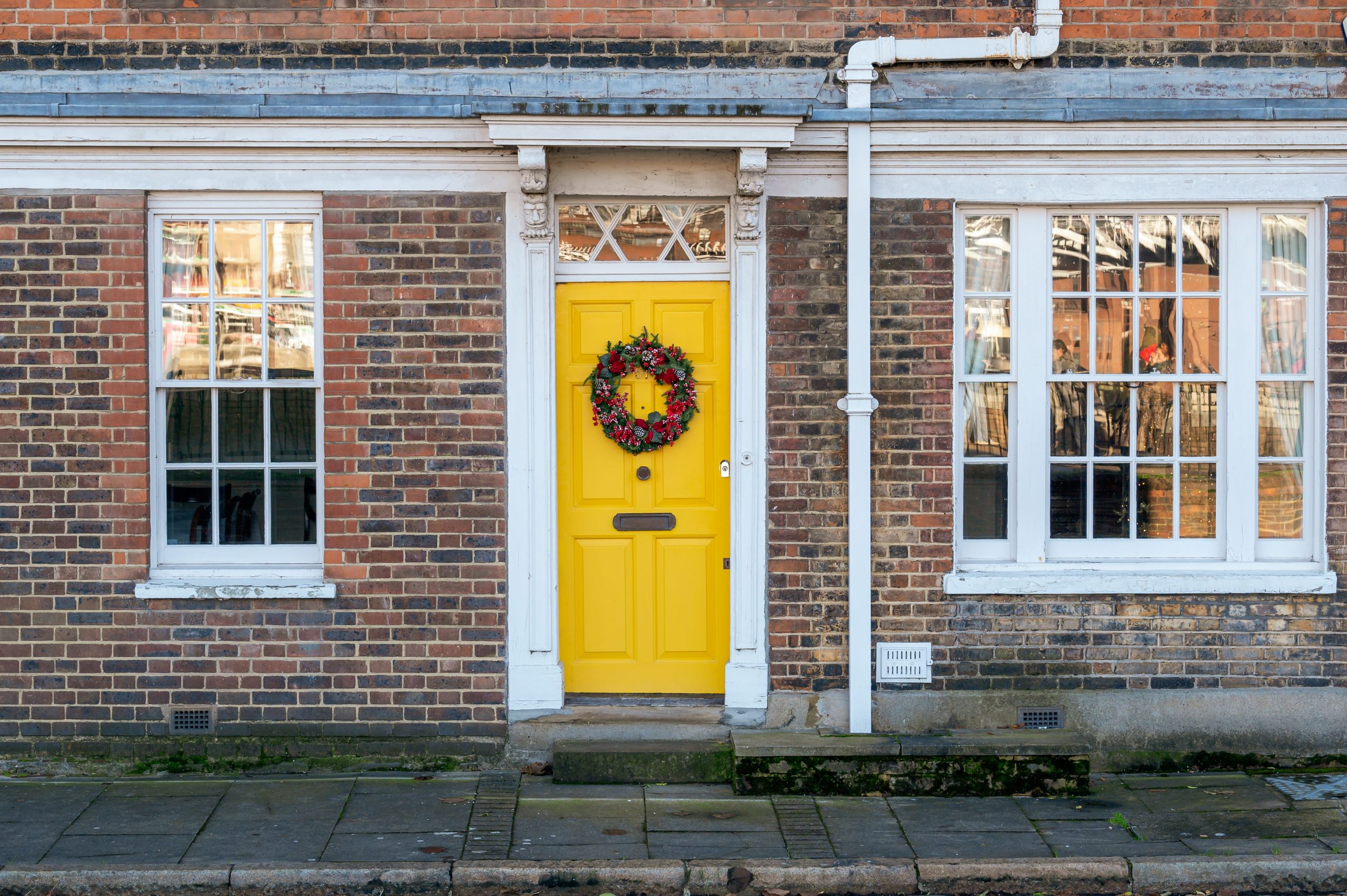 Charming yellow door adorned with a festive wreath, set in a classic brick facade on a quiet street.