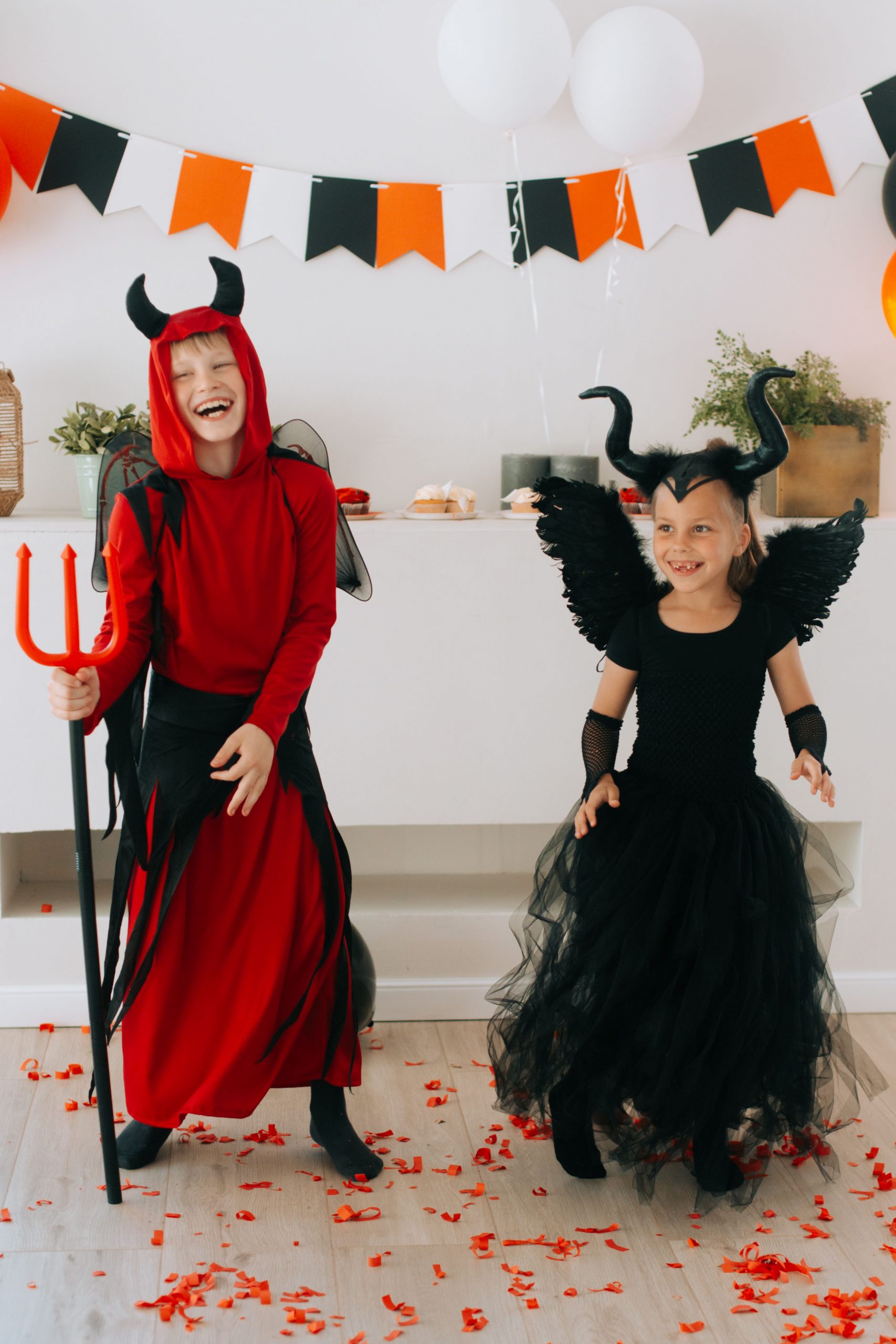 Children dressed as a devil and a demon laughing during a Halloween party indoors.