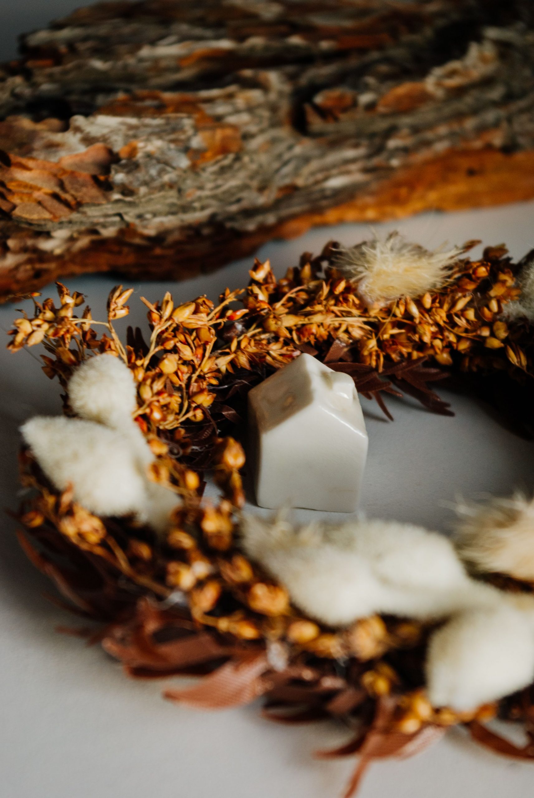 Close-up of an autumn wreath with bark and a ceramic house, emphasizing rustic decor.