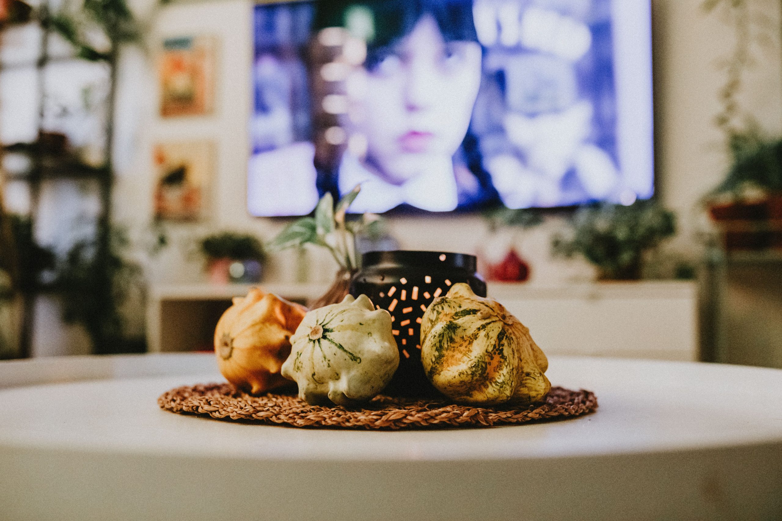 Close-up of decorative gourds on a table with a TV background.