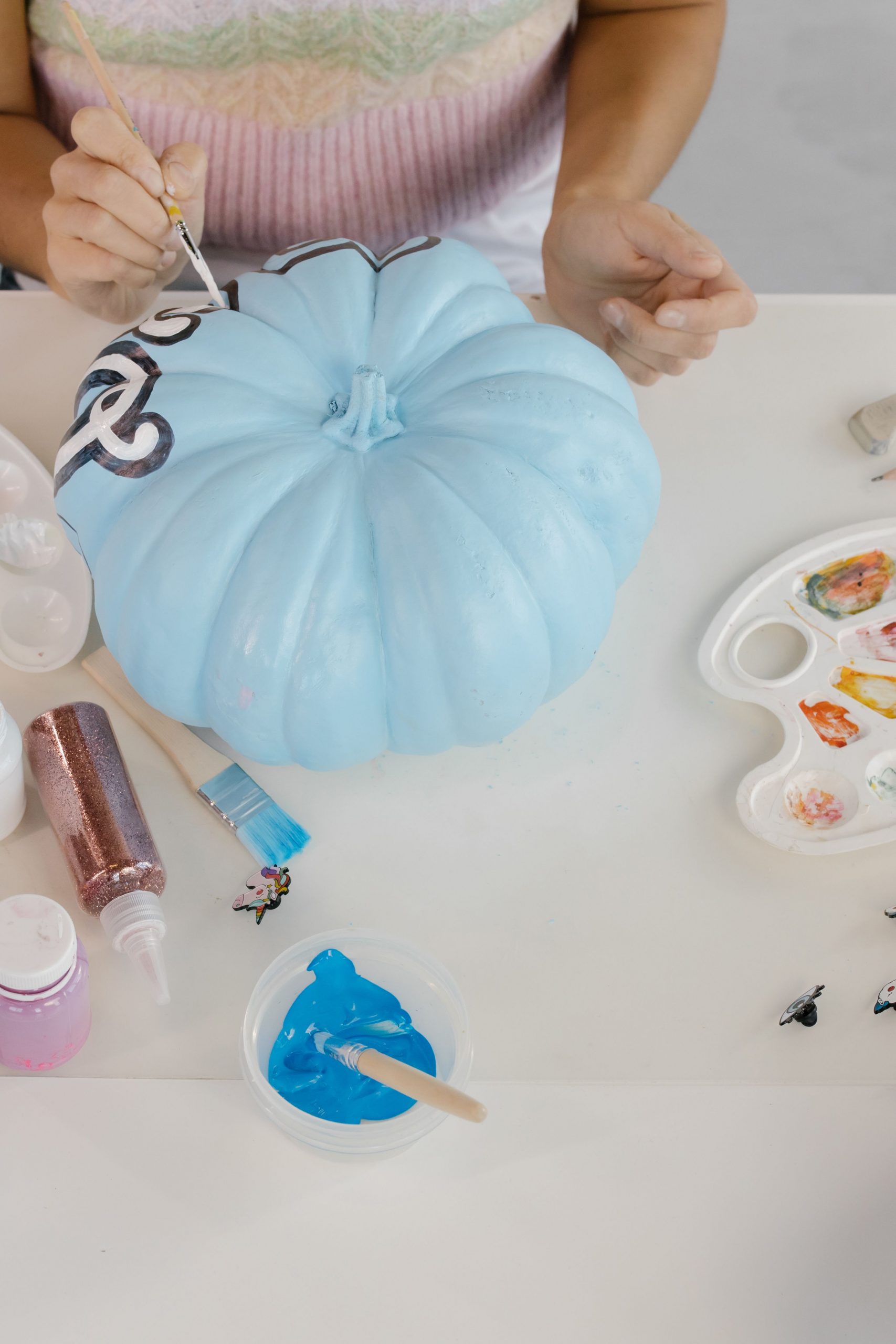 Close-up of painting a blue pumpkin with art materials for Halloween decor.