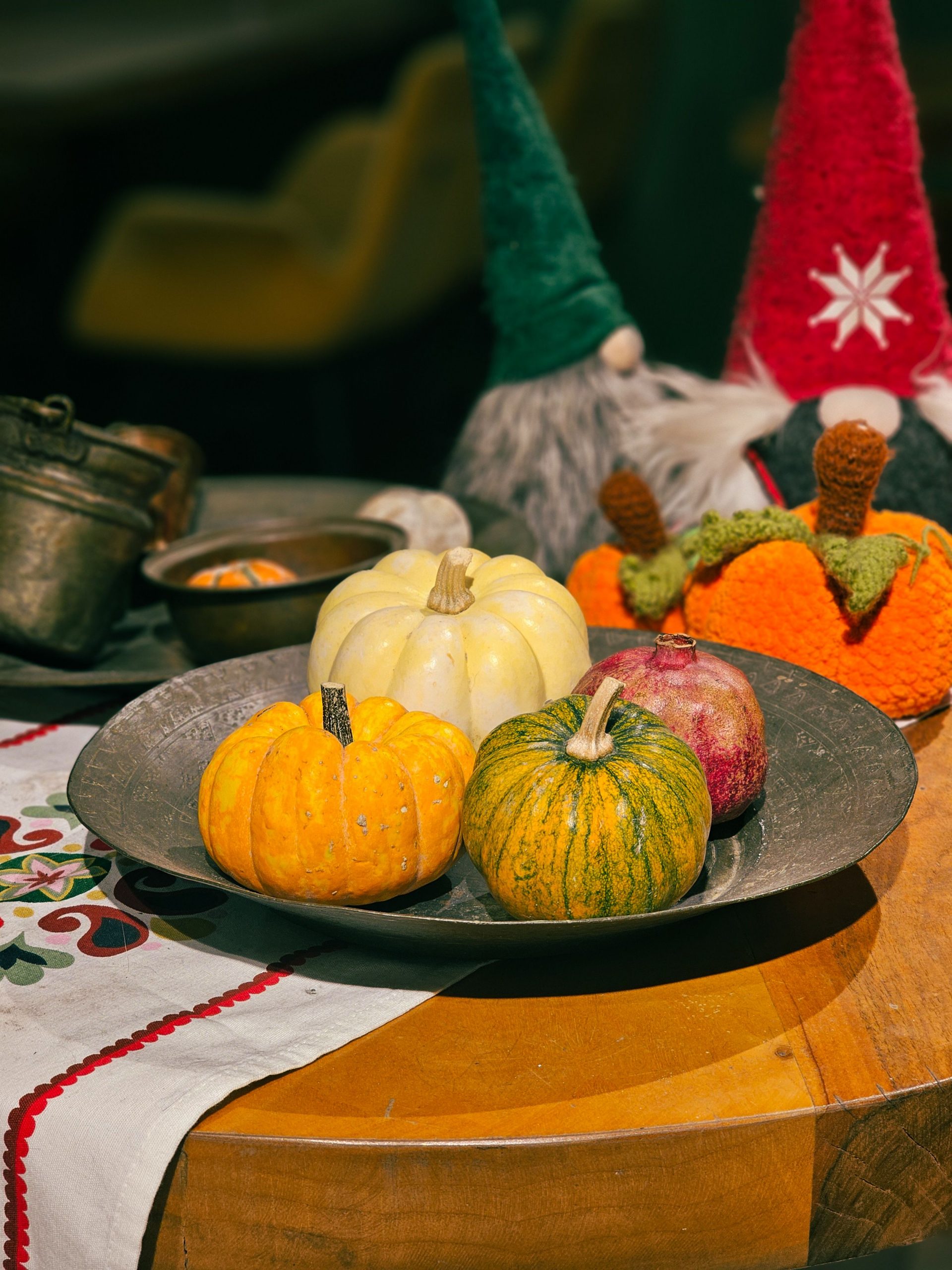 Colorful autumn scene with pumpkins on an ornate plate surrounded by festive gnomes and fall decor.