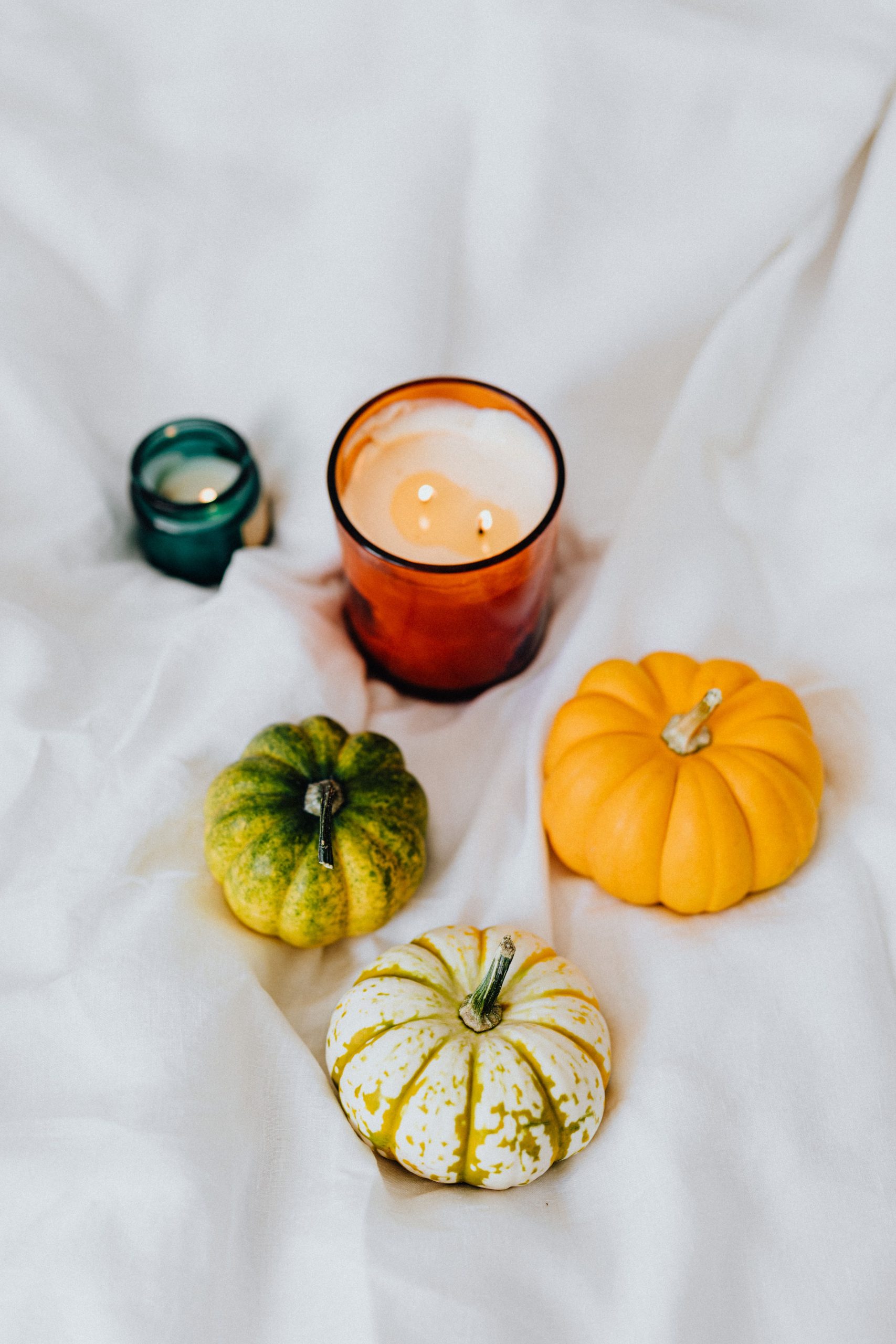 Cozy autumn scene featuring pumpkins and candles on a white textile.