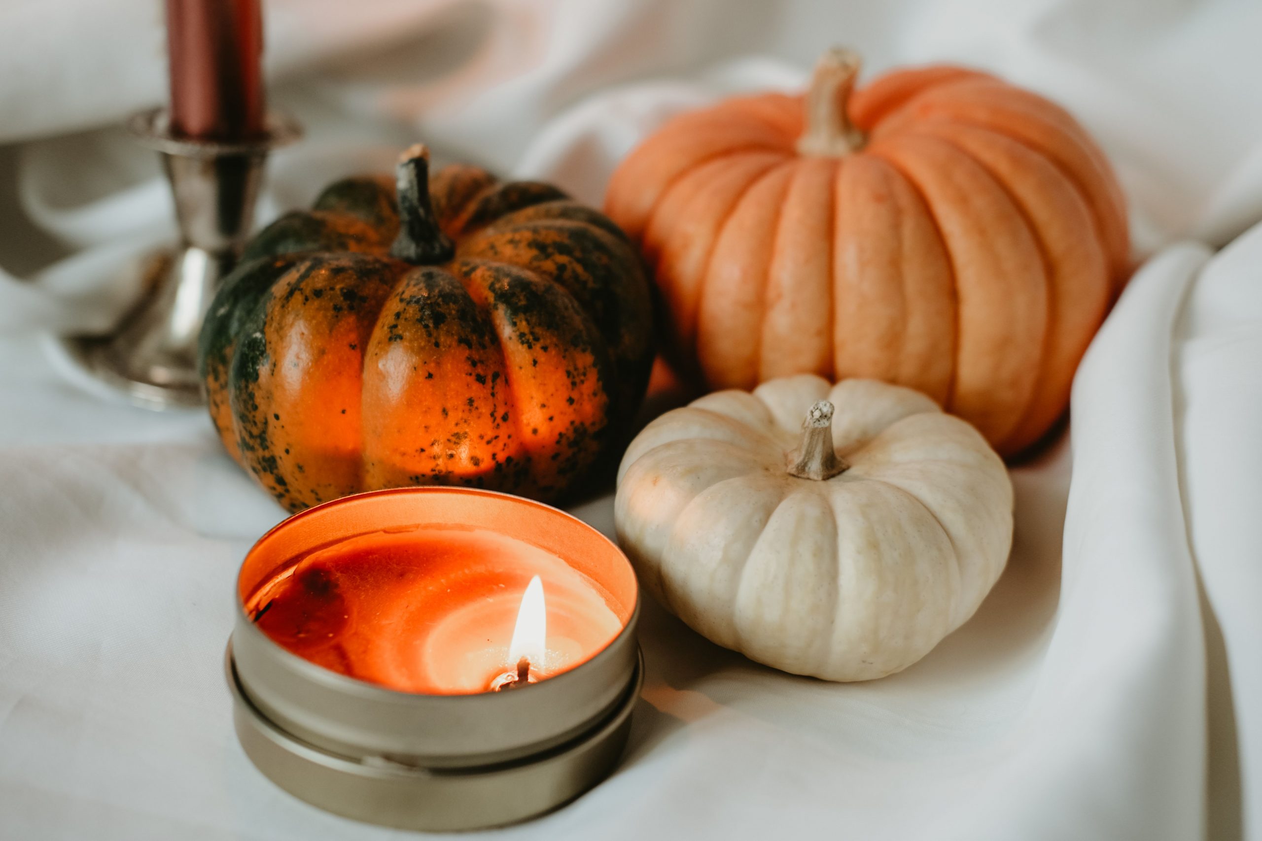 Cozy autumn scene with pumpkins and a lit candle on a soft white fabric, perfect for fall themes.