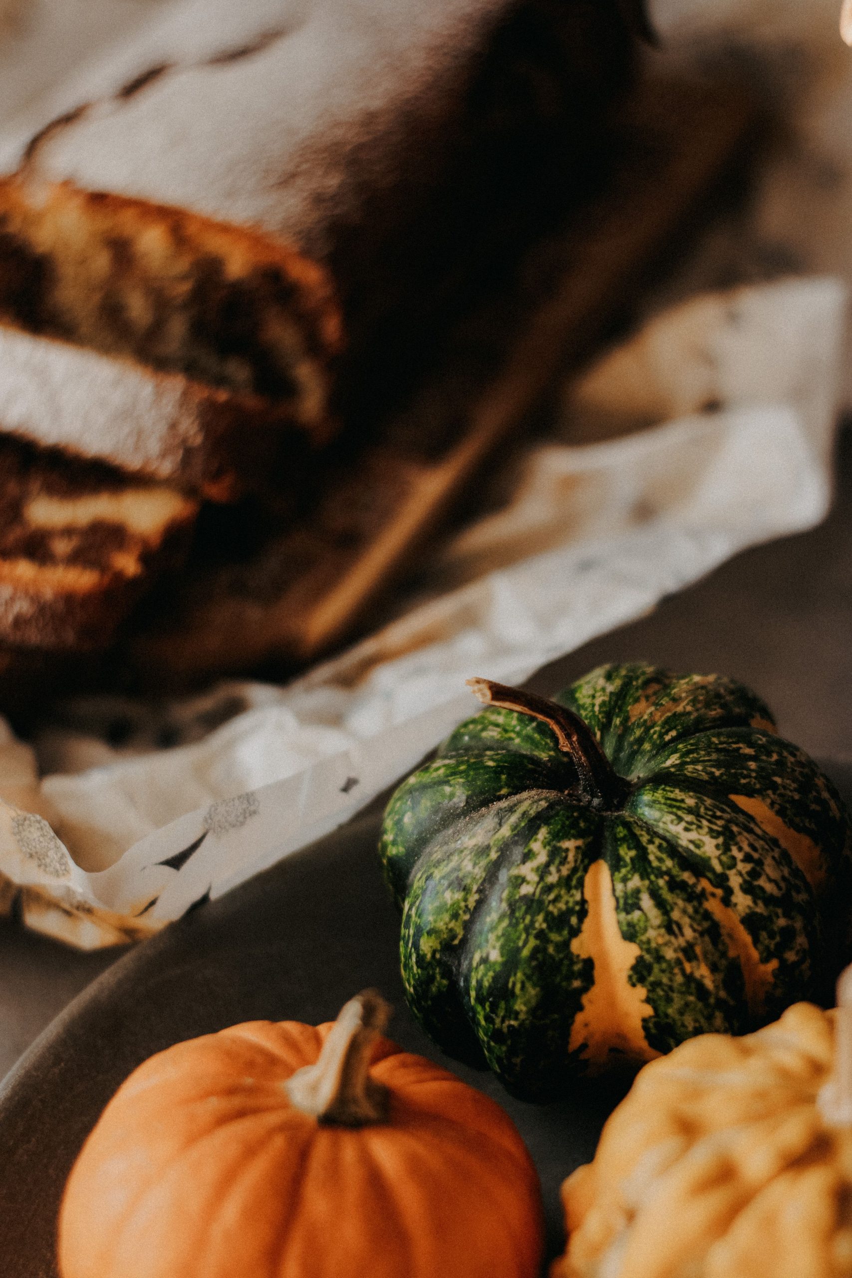 Cozy autumn still life featuring sliced pumpkin bread and decorative gourds on a table.