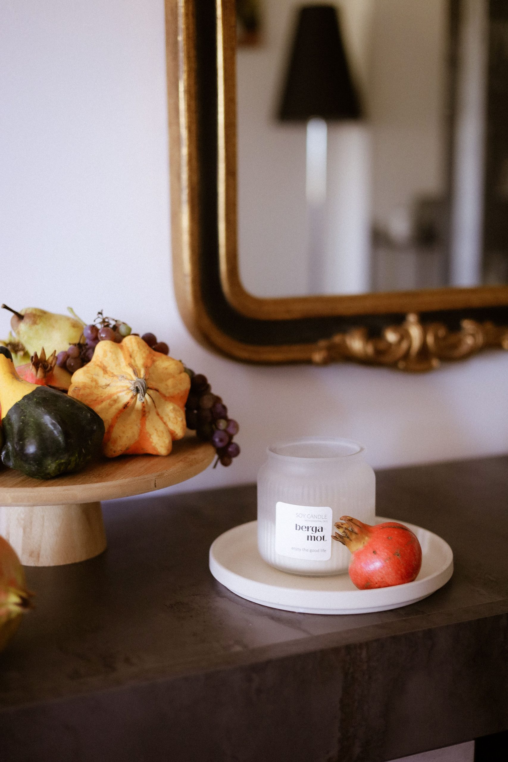 Cozy tabletop decor featuring a candle, gourds, and fruits in an elegant setting.