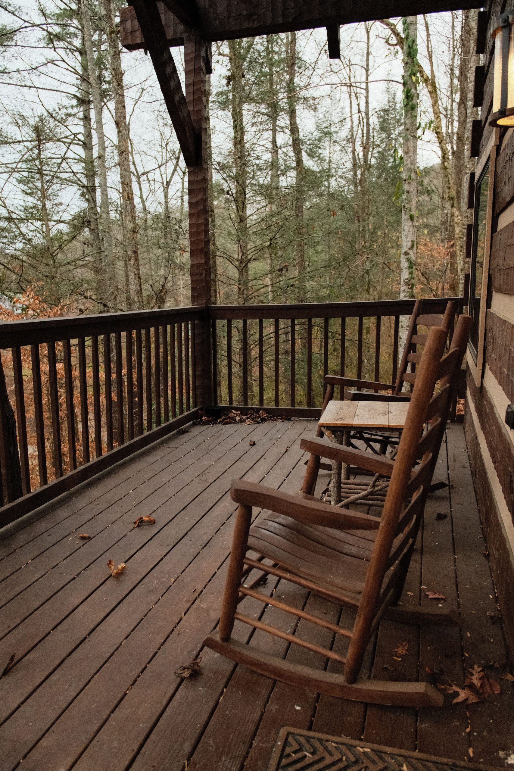 Cozy wooden deck with rustic chairs overlooking a peaceful forest in autumn.