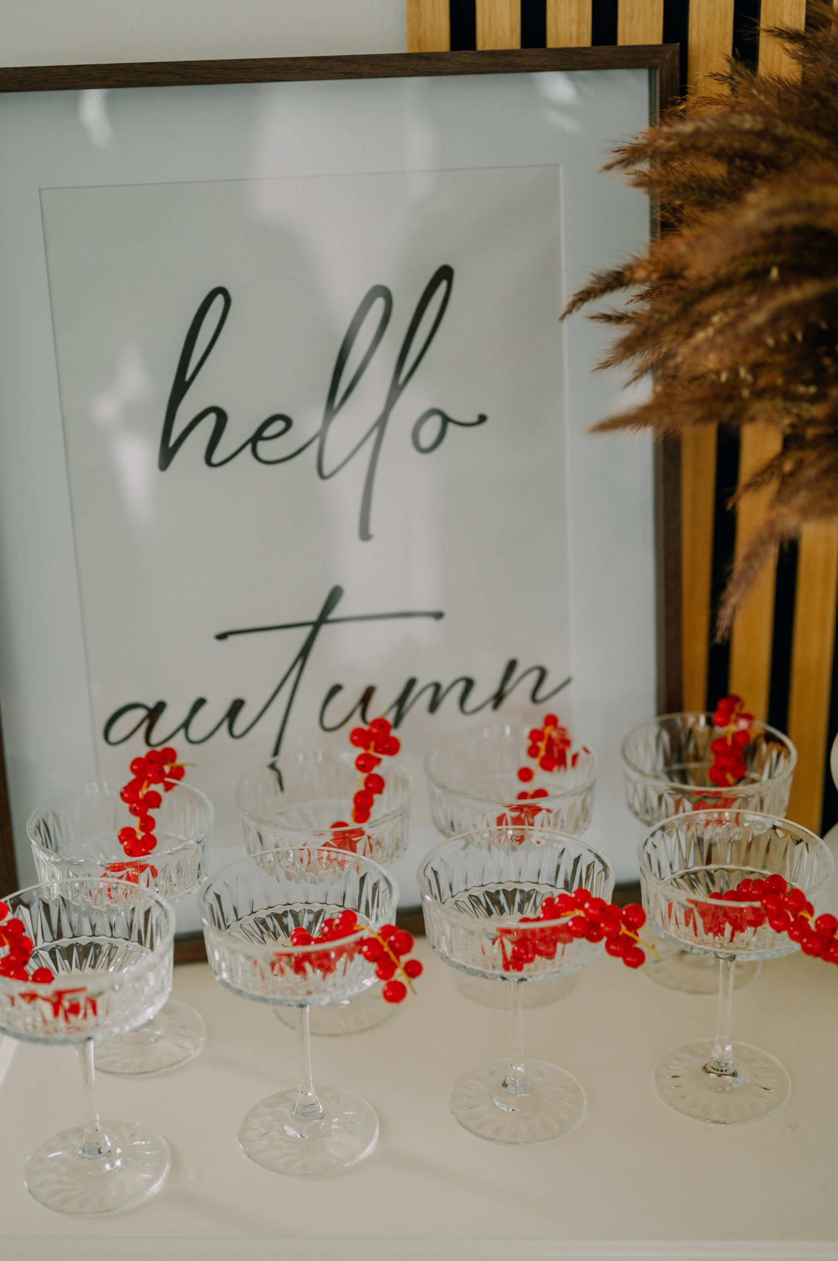 Decorative autumn-themed setup with glassware, red berries, and 'hello autumn' sign.