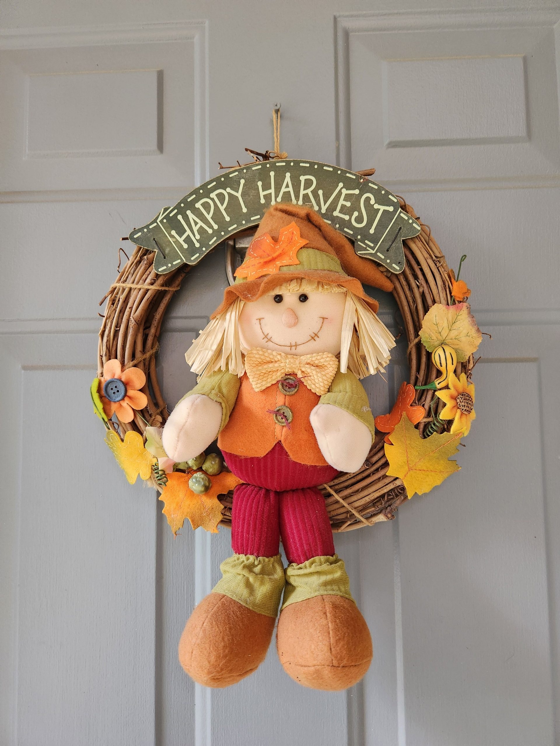 Decorative autumn wreath with a cheerful scarecrow and fall leaves, perfect for welcoming guests.