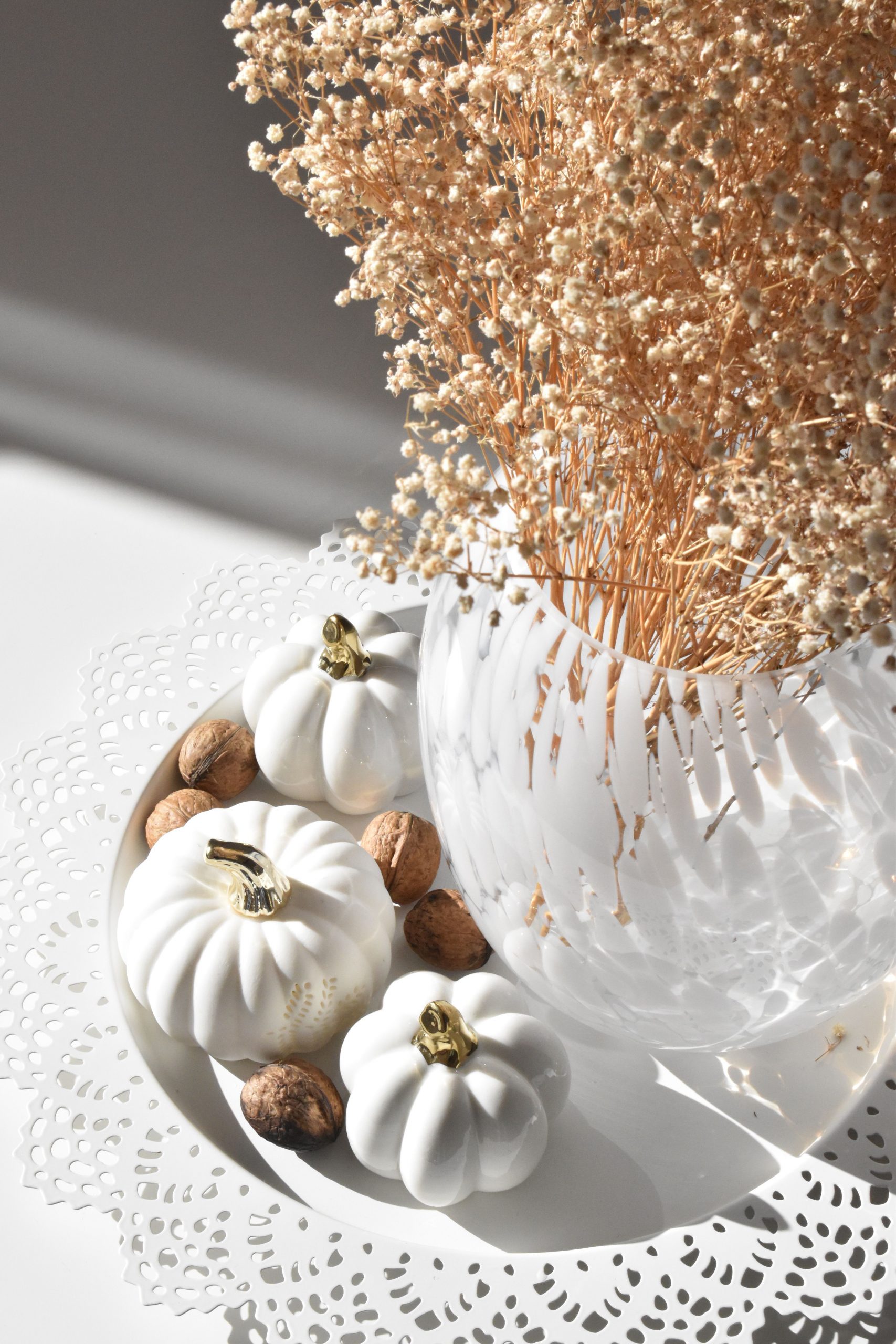 Elegant autumnal arrangement with white pumpkins, dried flowers, and walnuts in soft lighting.