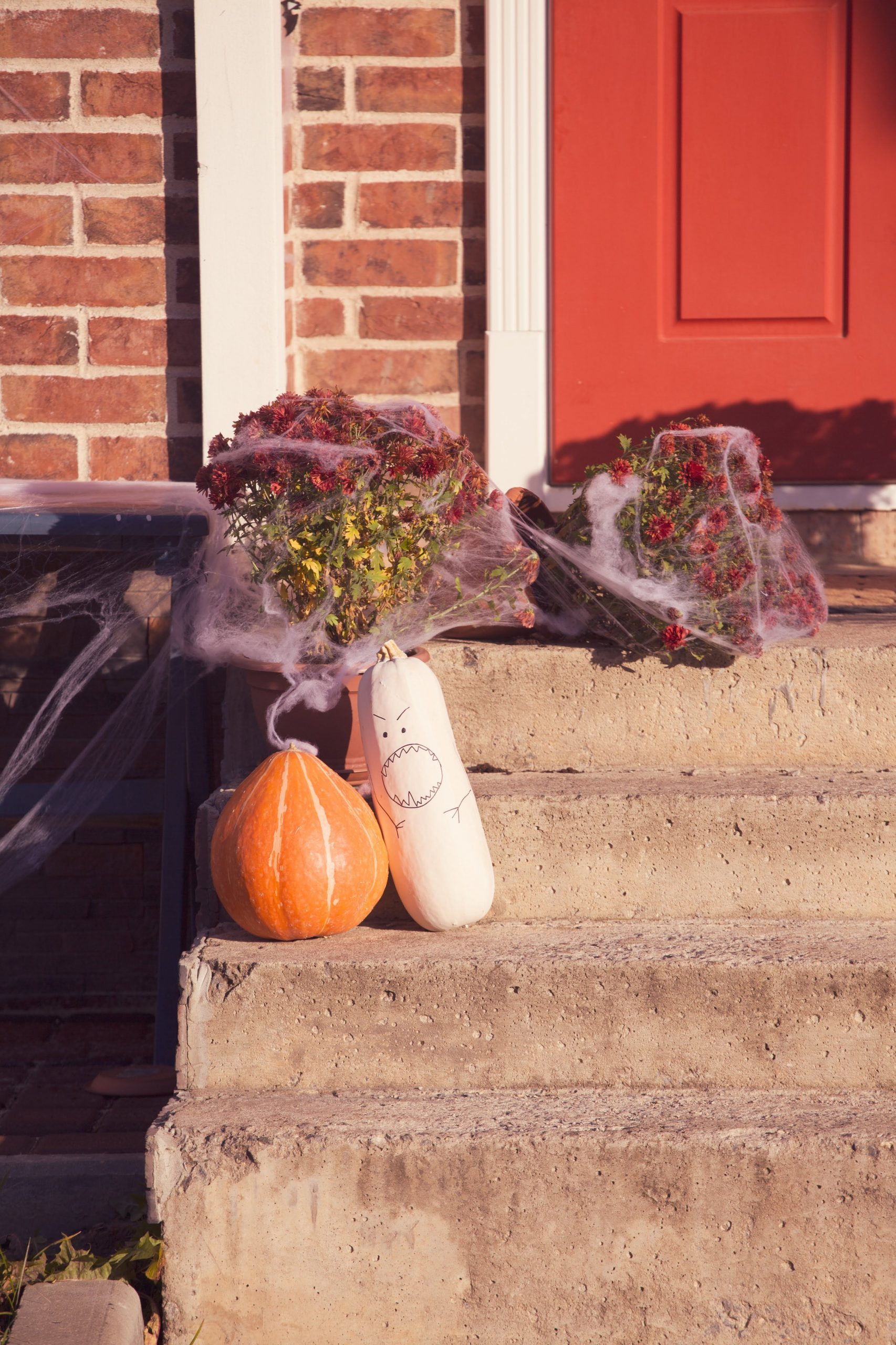 Festive Halloween decor with pumpkins and spider webs on brick porch with red door.