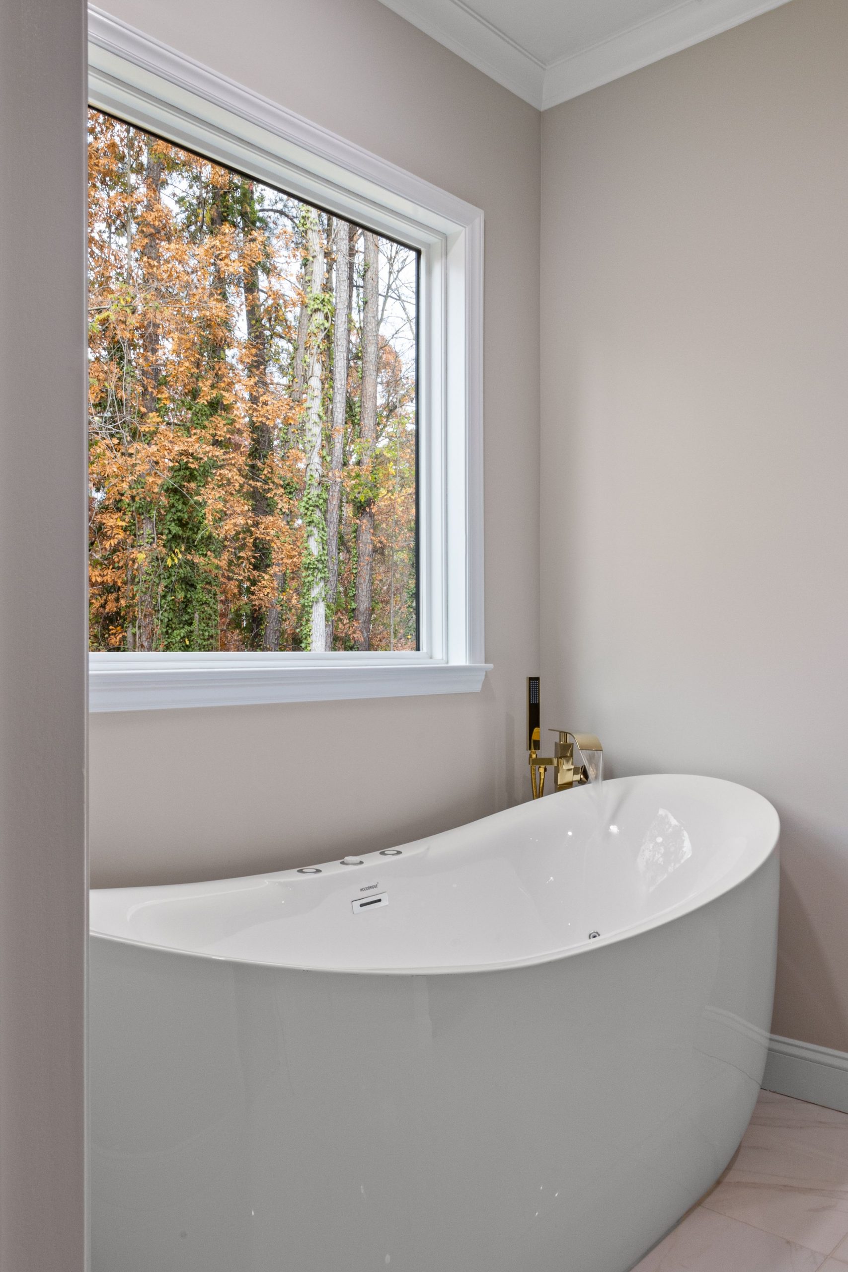 Freestanding bathtub in a contemporary bathroom with a view of autumn trees through large window.