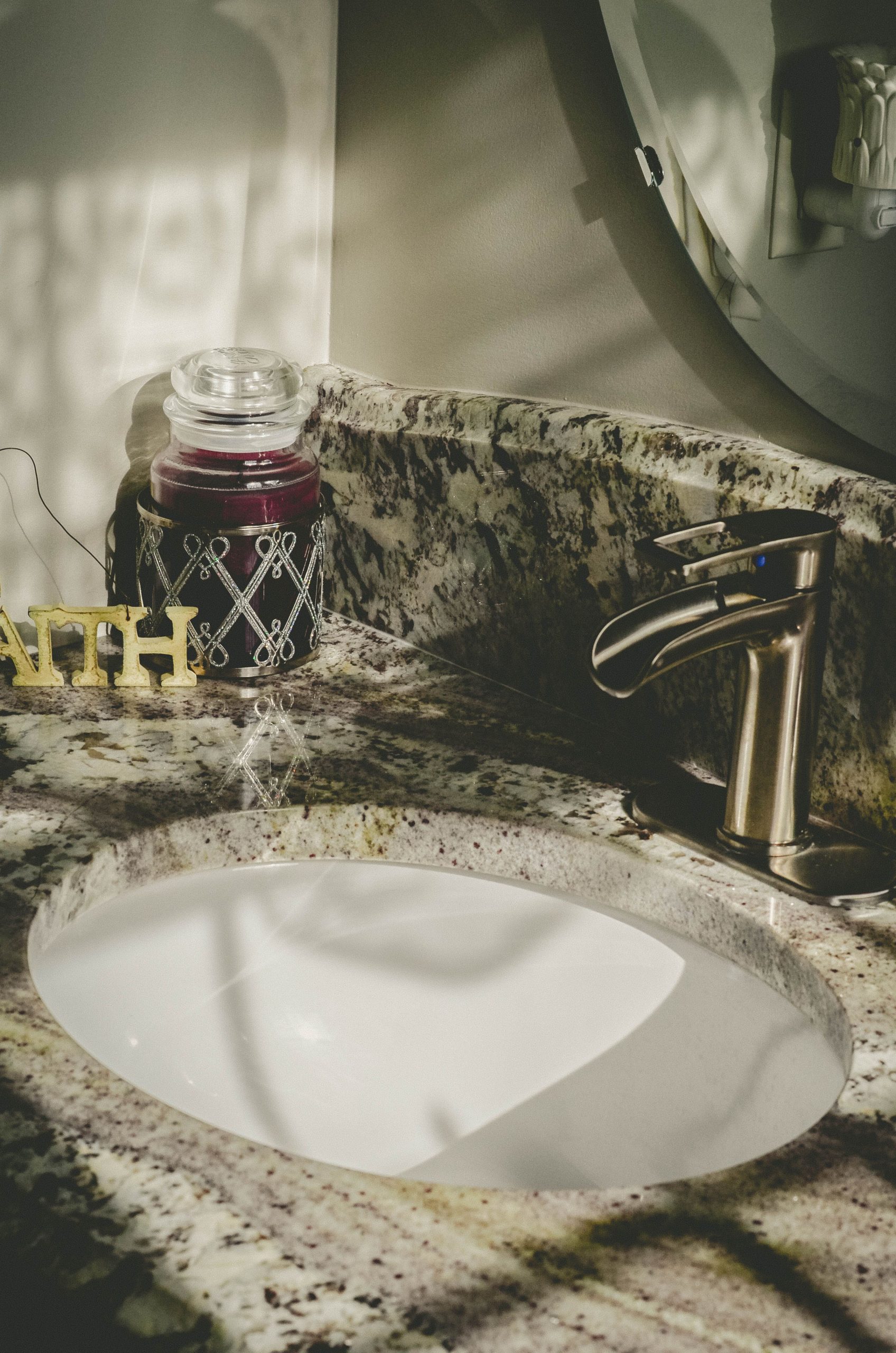 Granite bathroom sink with elegant faucet and decorative candle in soft daylight.