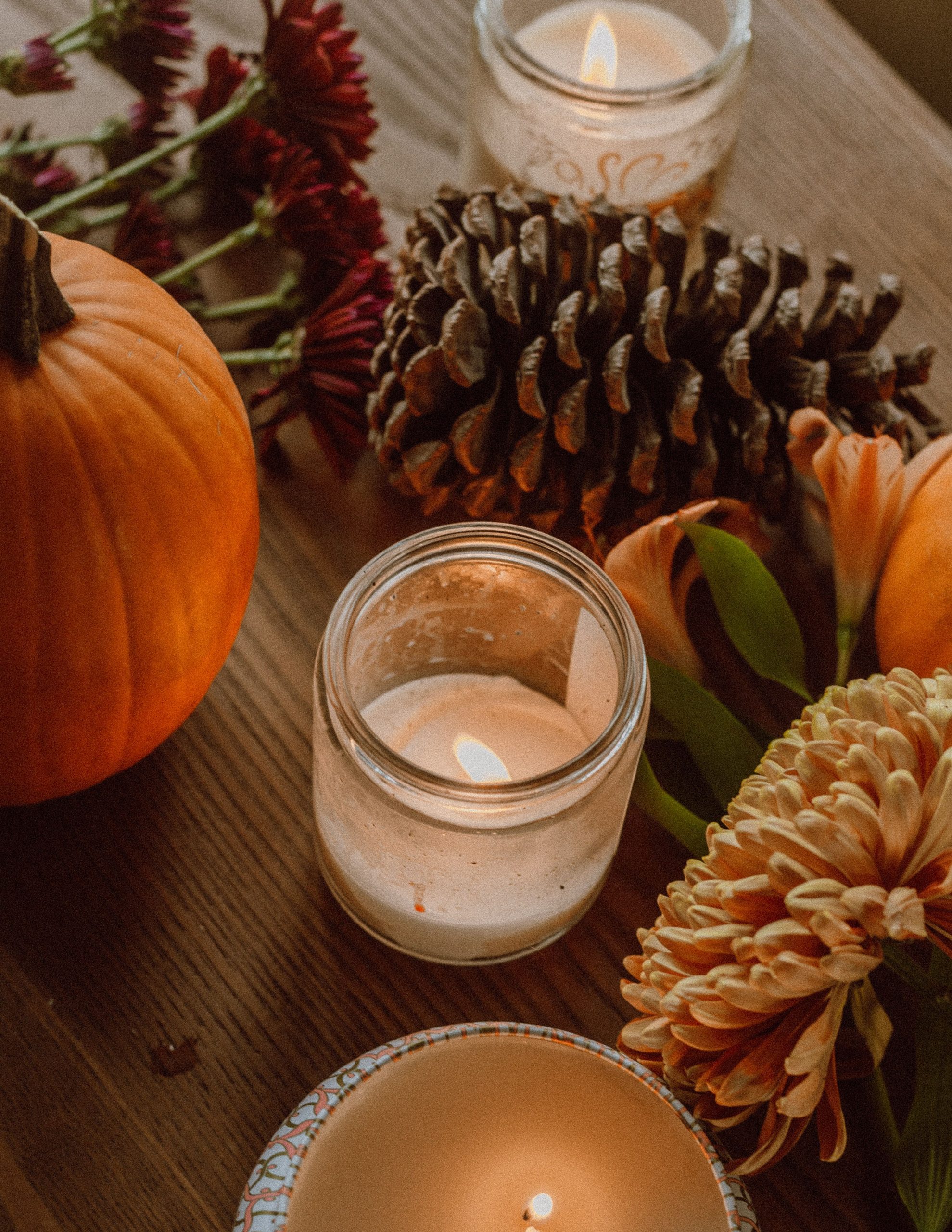 High angle composition of candleholders with burning tealights arranged on table near ripe pumpkin fir cone and flowers