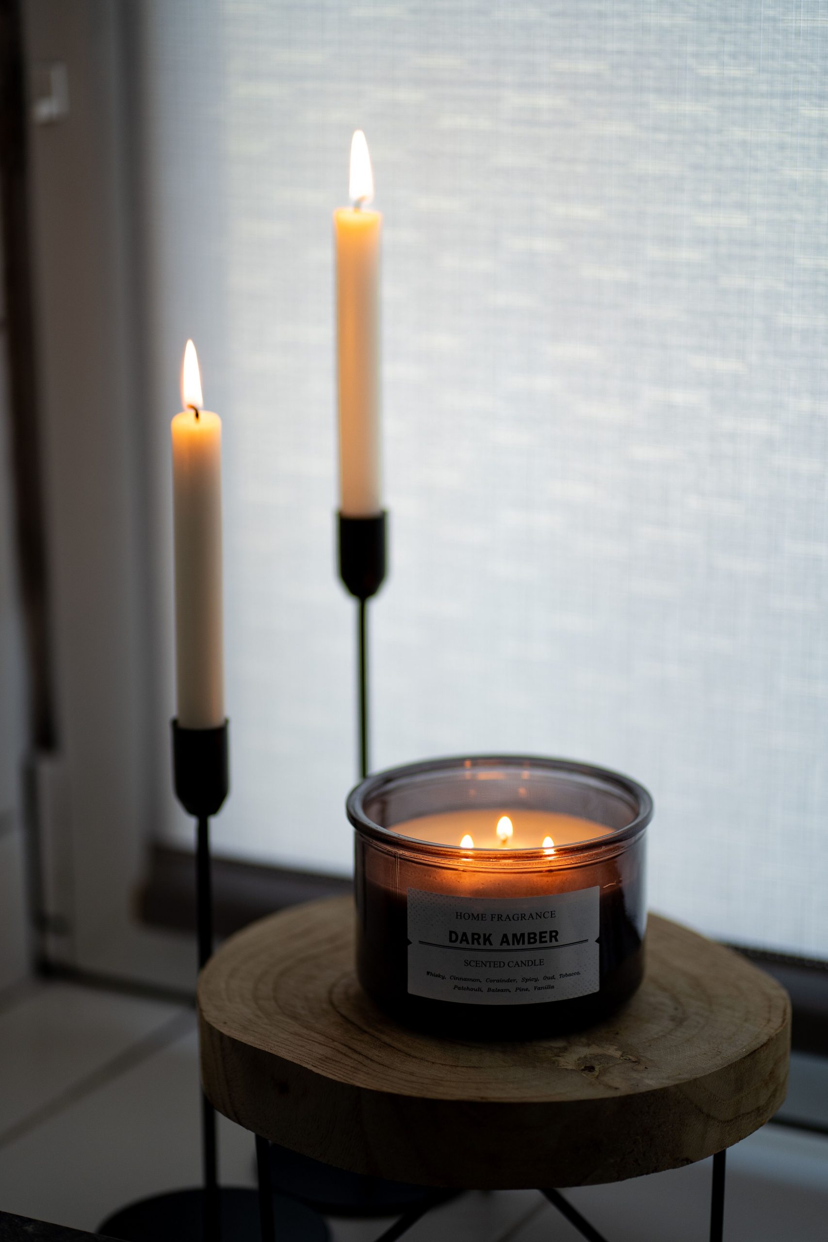 Illuminated dark amber candle with elegant candlesticks creating a warm ambiance indoors.