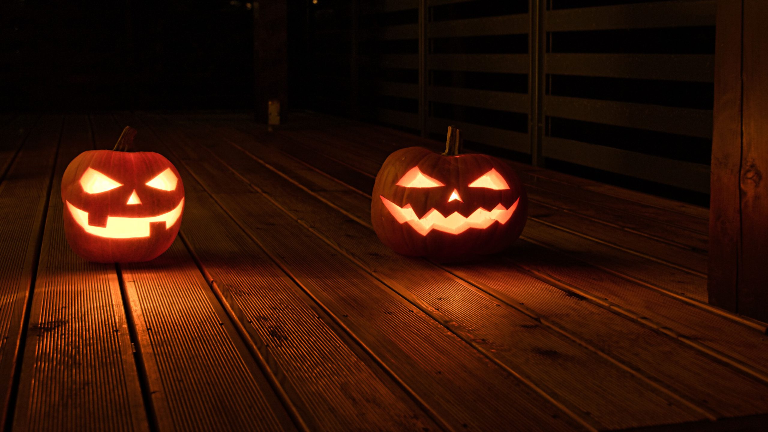 Illuminated jack-o-lanterns with carved faces create a spooky Halloween ambiance on a wooden deck at night.