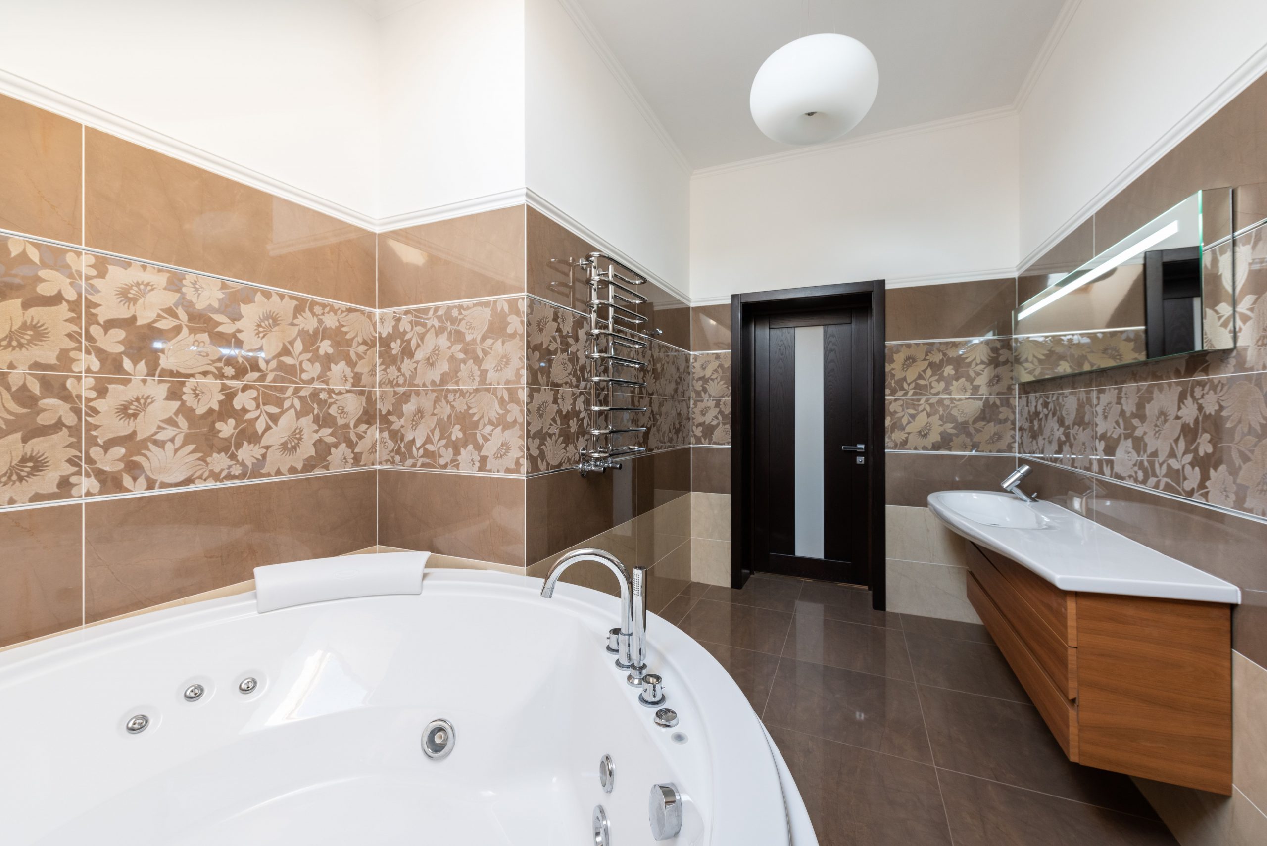 Interior of contemporary bathroom with round ceramic bathtub and sink and wooden cabinet in daytime