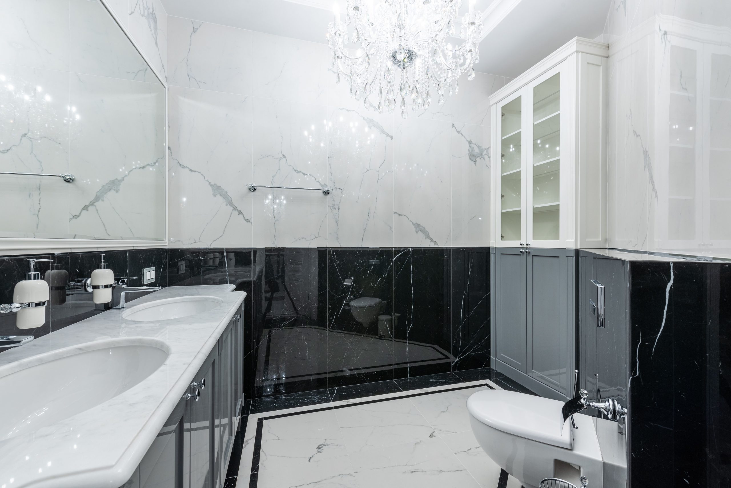 Interior of convenient modern bathroom with white clean sinks and toilet under glowing chandelier