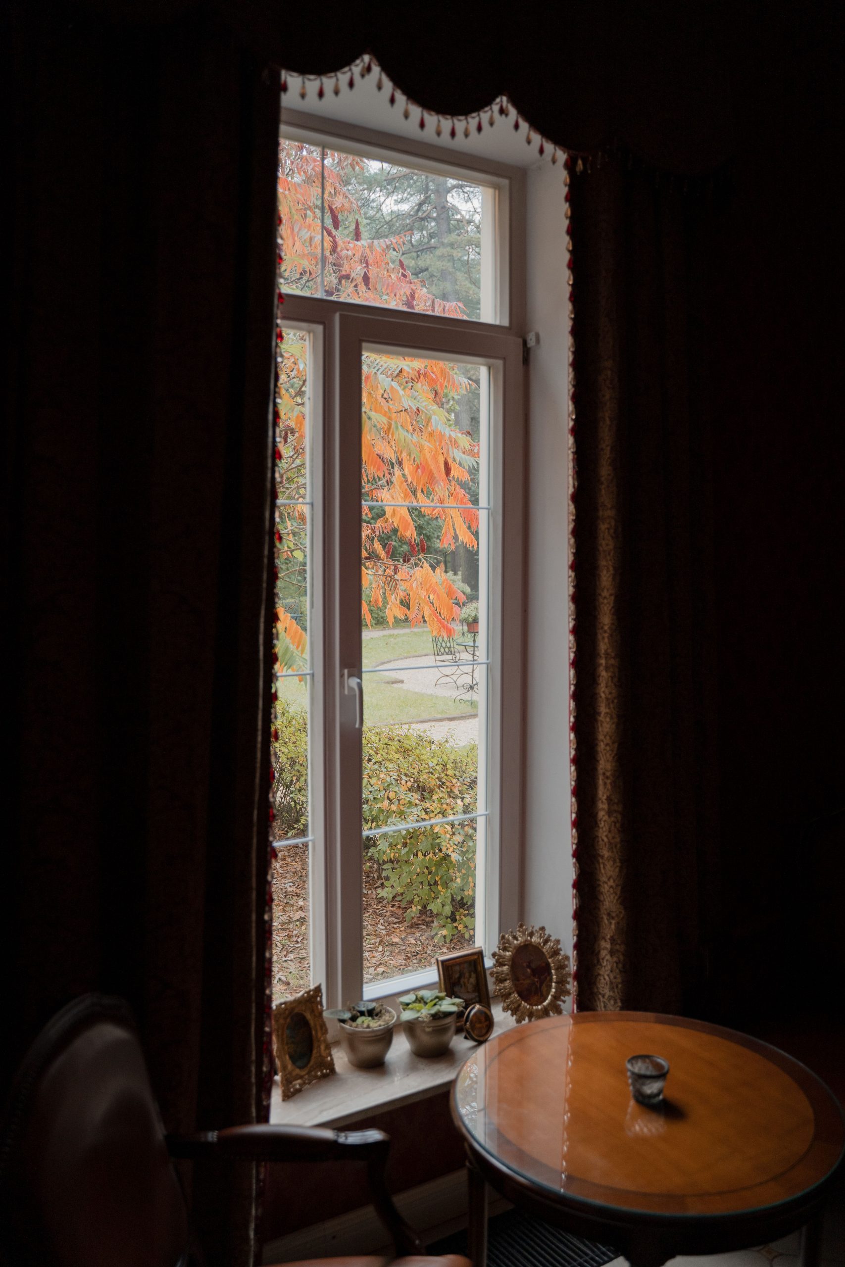 Interior room with warm decor overlooking a vibrant autumn scene through a large window.