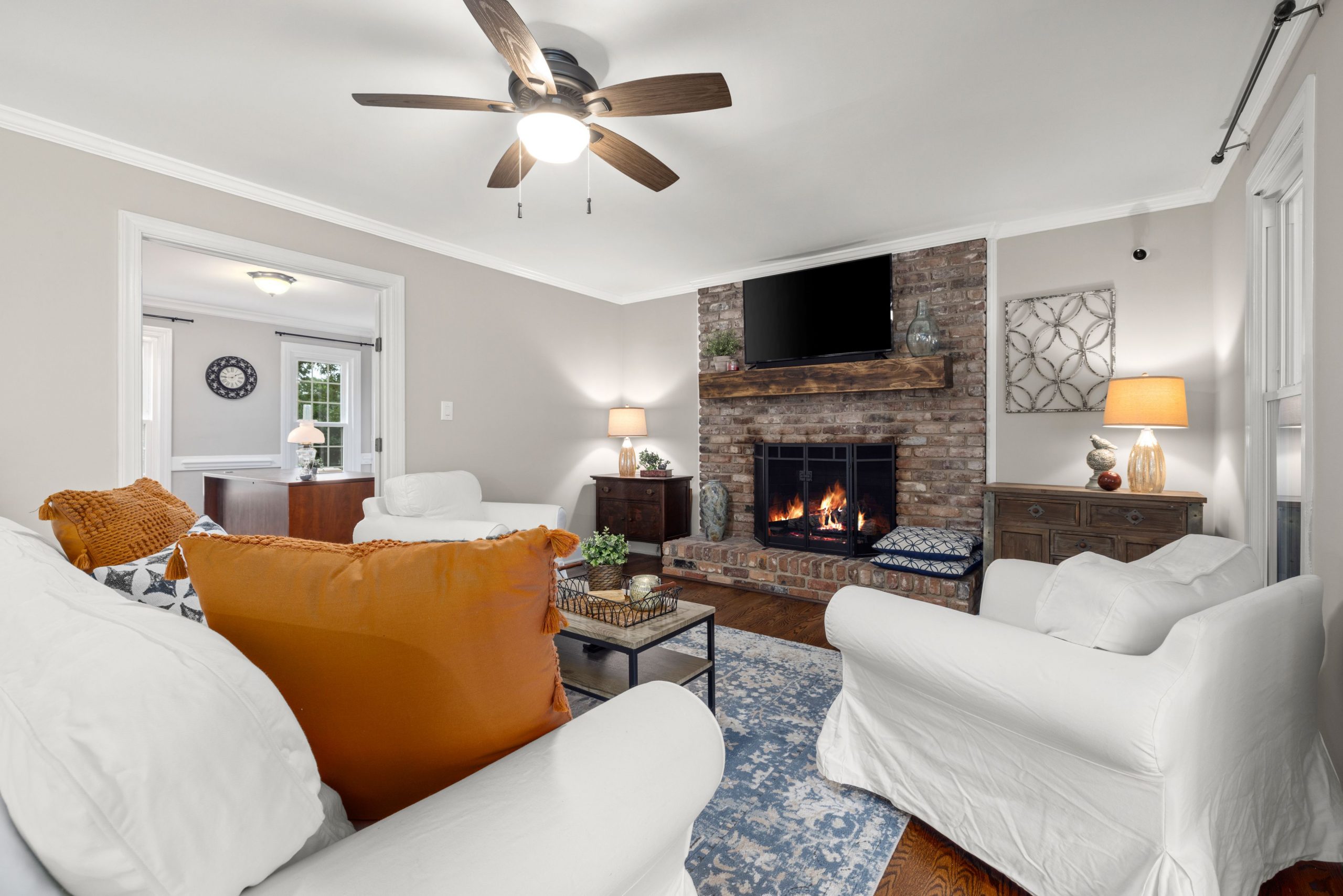 Inviting living room with a warm brick fireplace, orange accents, and classic decor.