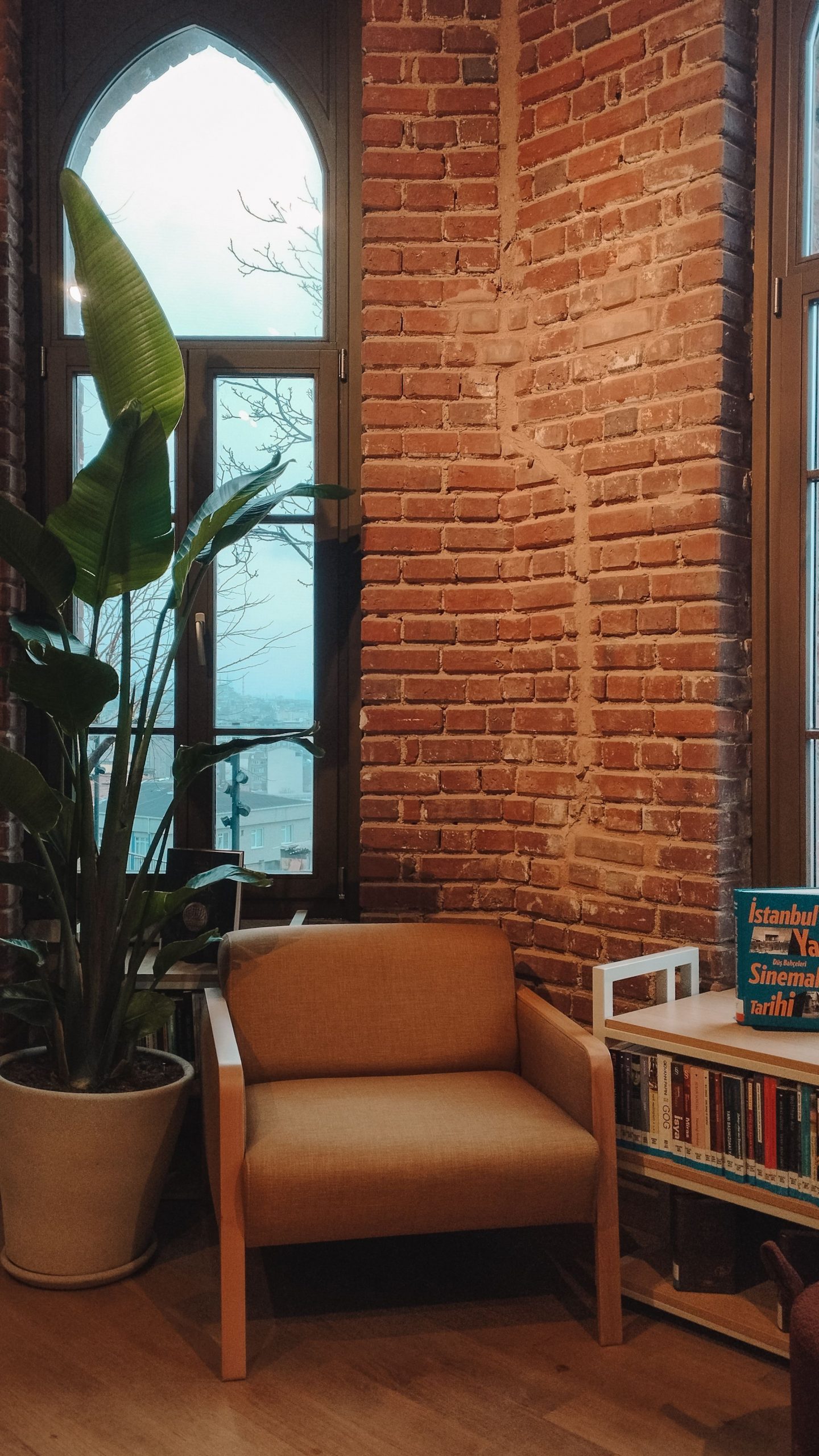 Inviting living space with a comfortable chair, books, and large windows against a brick wall.