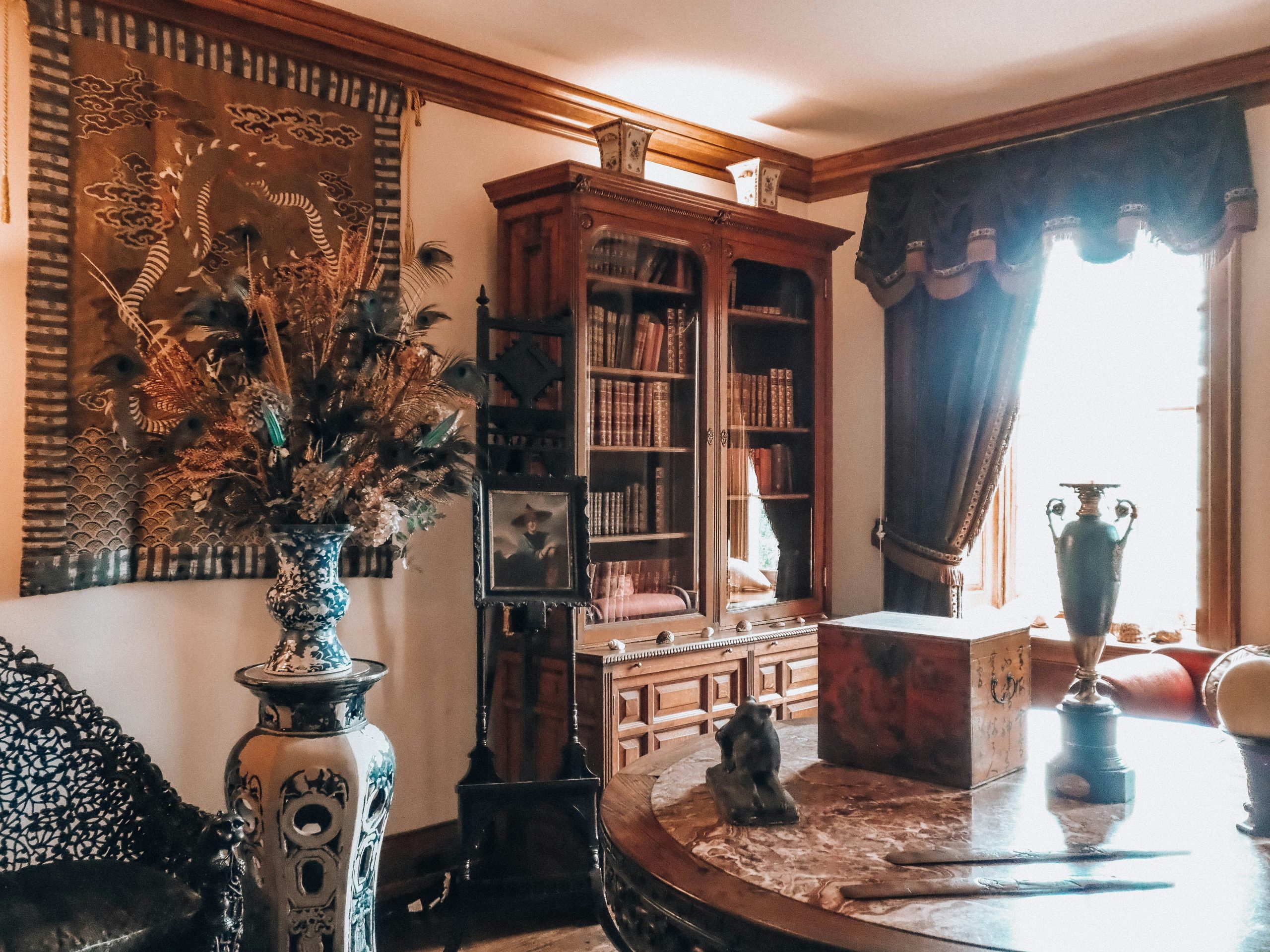 Ornate antique room with a bookshelf, vase, and wall tapestry.