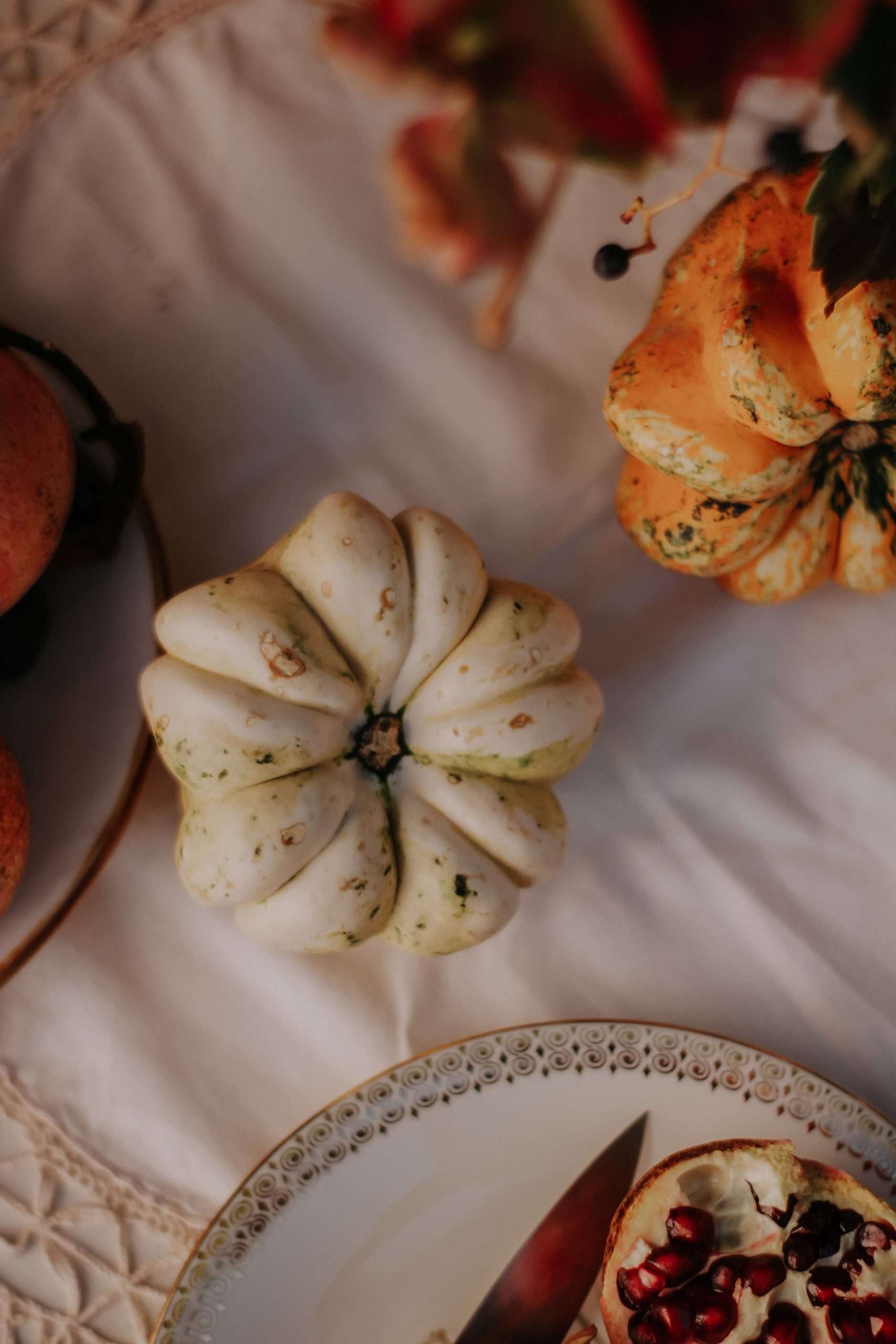 Overhead shot of colorful gourds and pomegranate on a table setting.