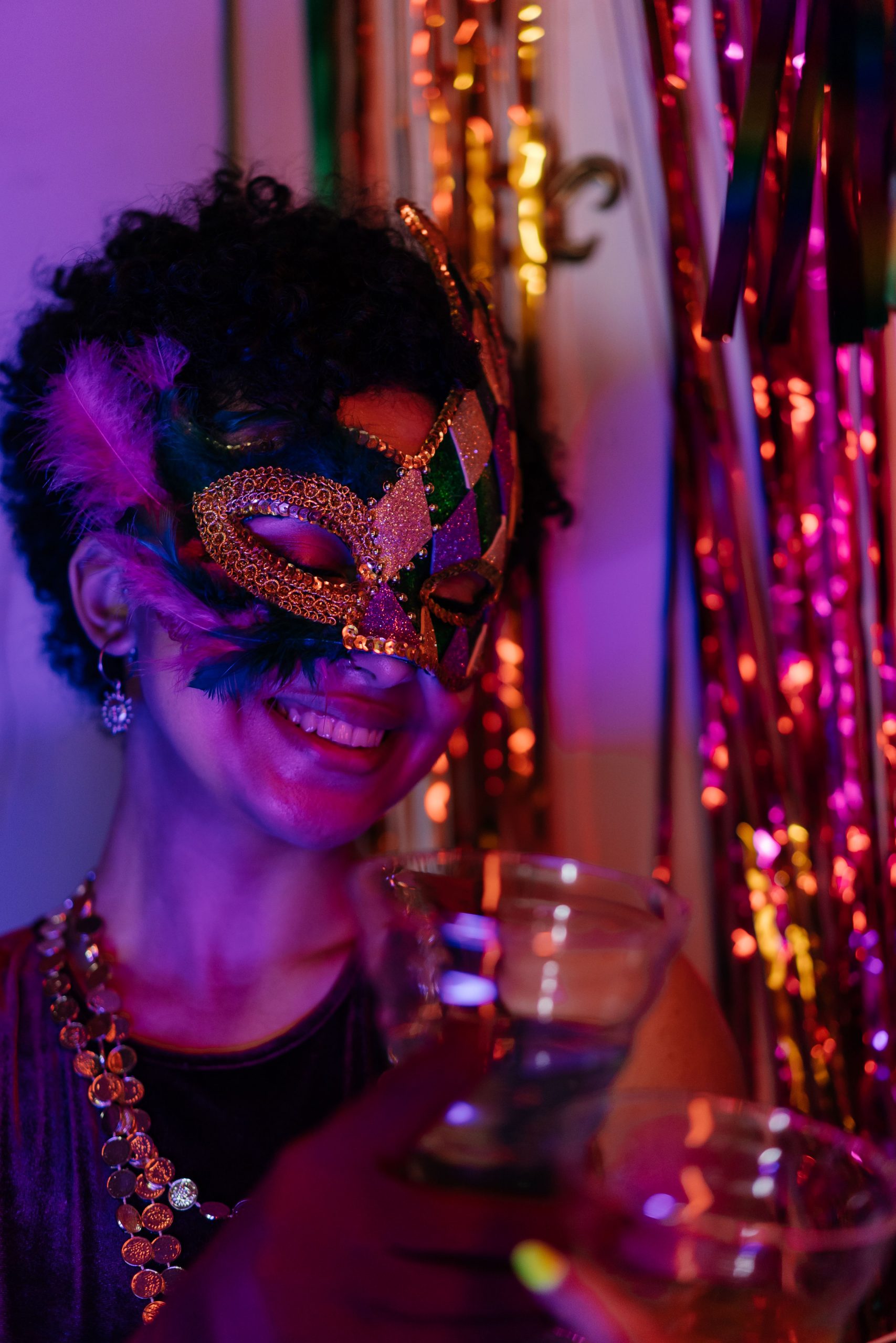 Smiling woman in festive mask enjoying a celebration with drinks.