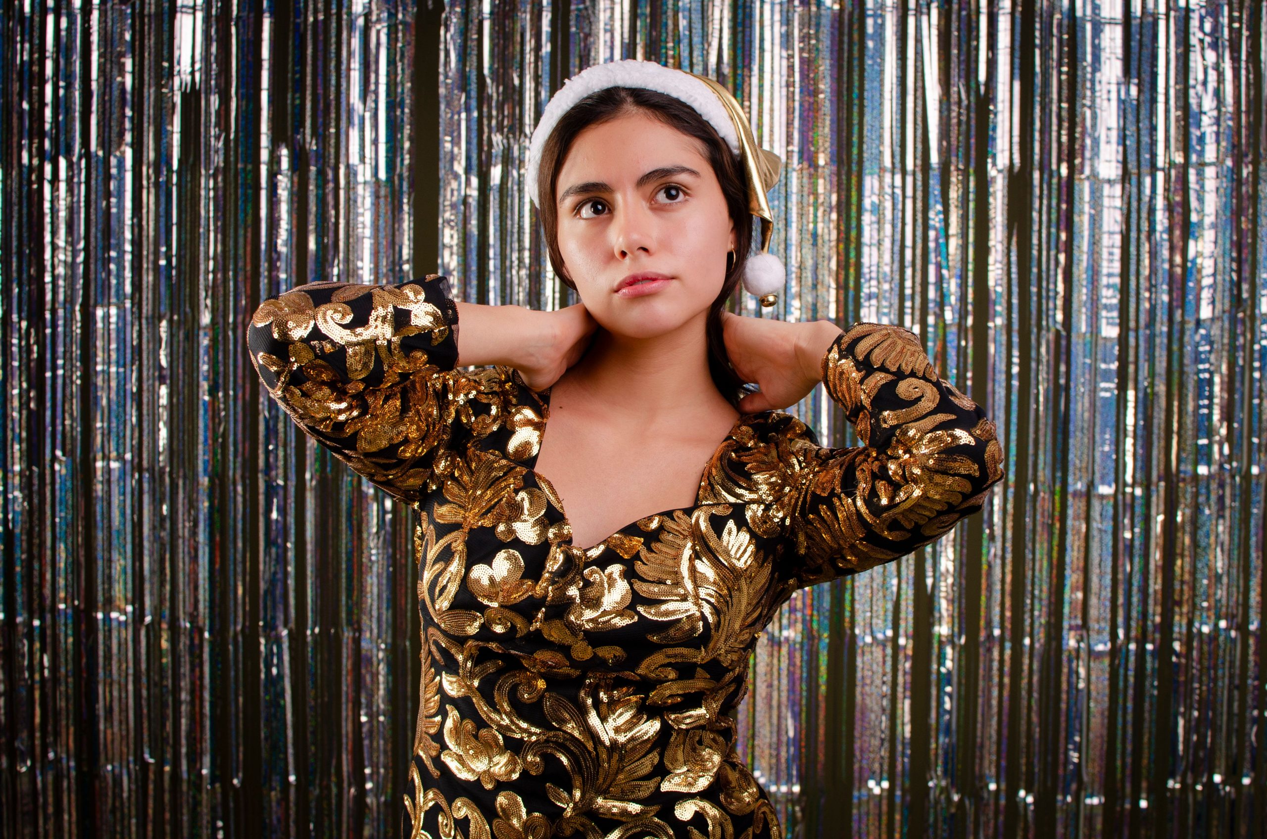 Sophisticated holiday portrait of a woman in a gold dress and Santa hat, ready for celebration.